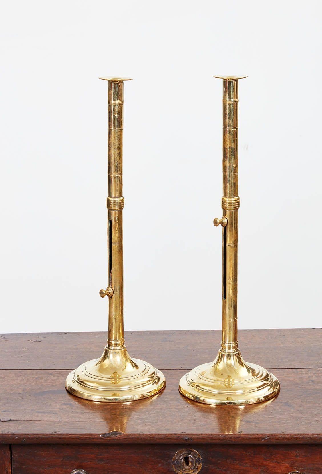 A pair of brass adjustable candlesticks having tall shafts with slide adjuster knob and mid-shaft ring turnings, surmounted by drip guard and standing on turned base. English, circa 1830.