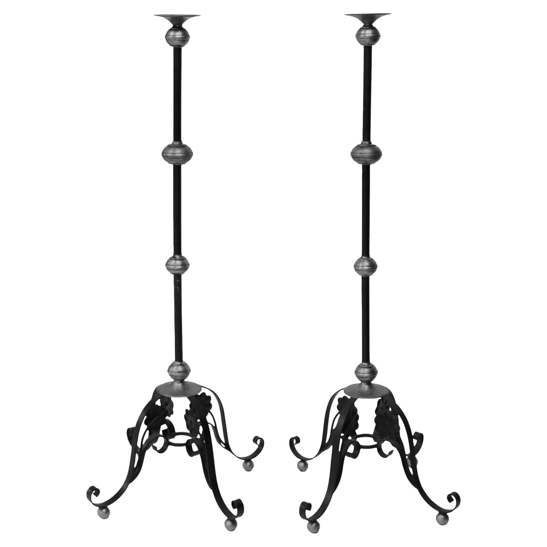A pair of brass and wrought iron Church Torchères candle floor stands, 20th c. The candle stands each feature a brass bobeche, iron stand, rising on scroll legs with flower heads, ending in ball feet. 

Dimensions
approx 58.75