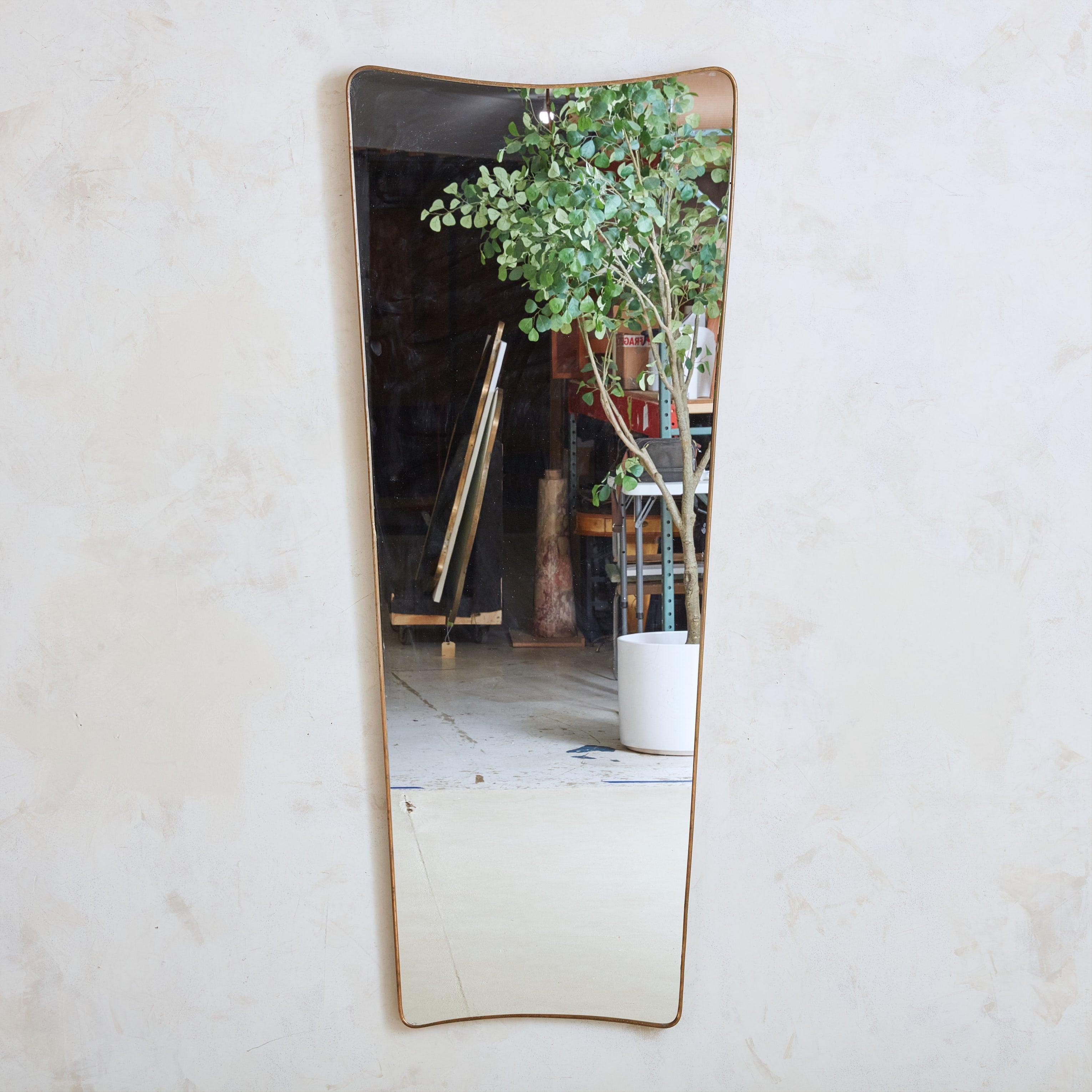 Un alto specchio da parete italiano a forma di scudo con curve sottili e bordi arrotondati. La delicata cornice in ottone presenta una patina naturale e invecchiata. Questo specchio ha un supporto in legno e include la ferramenta per appenderlo.