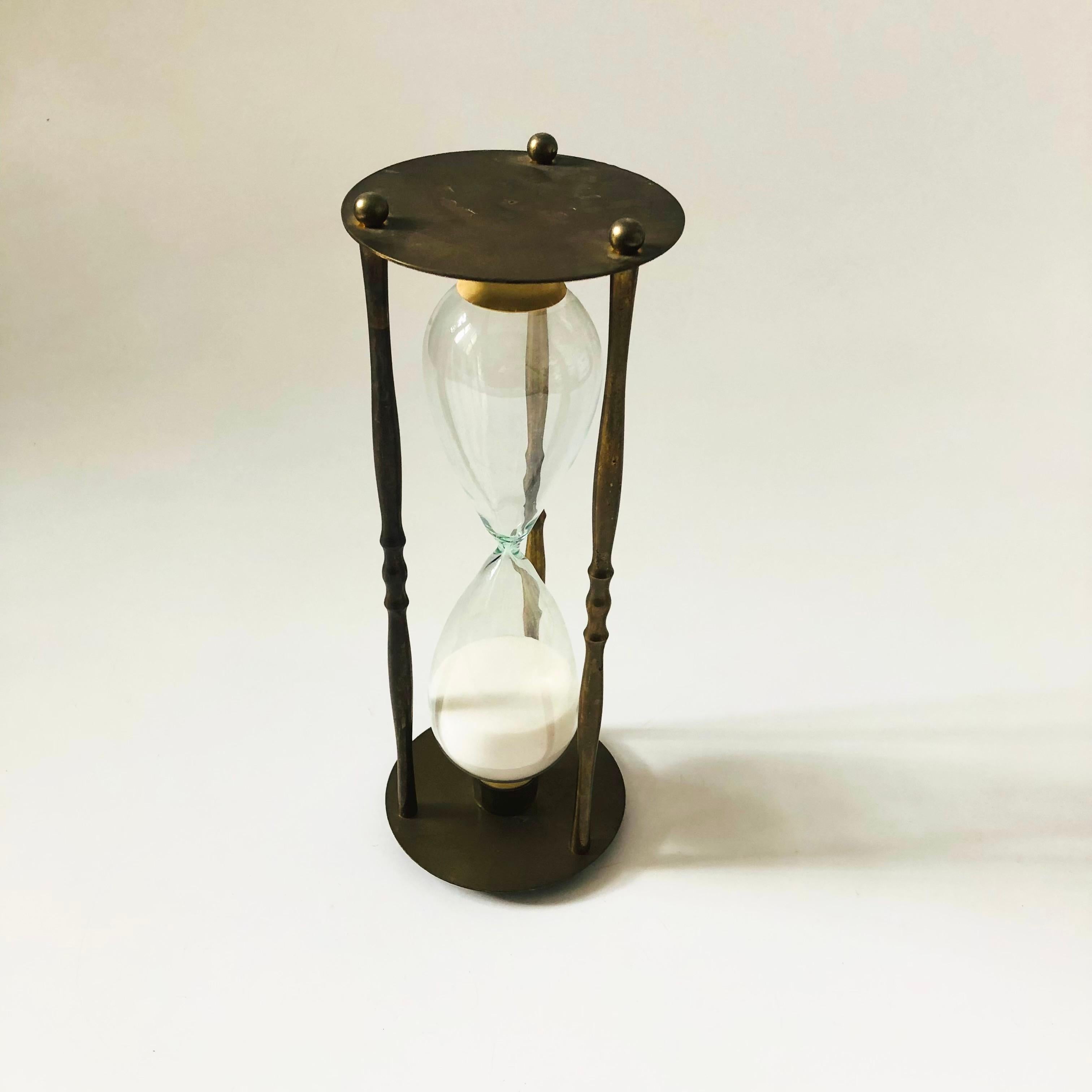 A large vintage brass and glass hourglass. Filled with white sand. Rubber fittings hold the glass in place.

