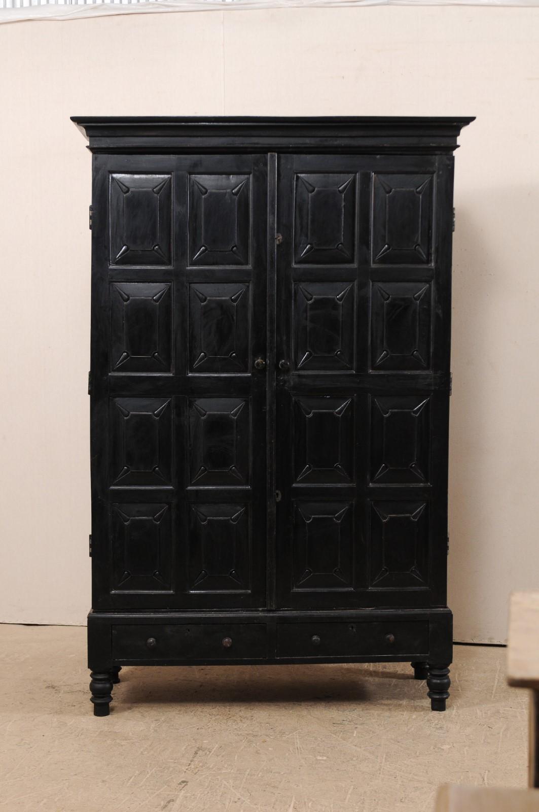 A tall British Colonial storage cabinet from the mid-20th century. This vintage cabinet features two decoratively carved raised eight-panel doors, revealing the interior shelving within, framed within a molded cornice at top, and plain skirt at