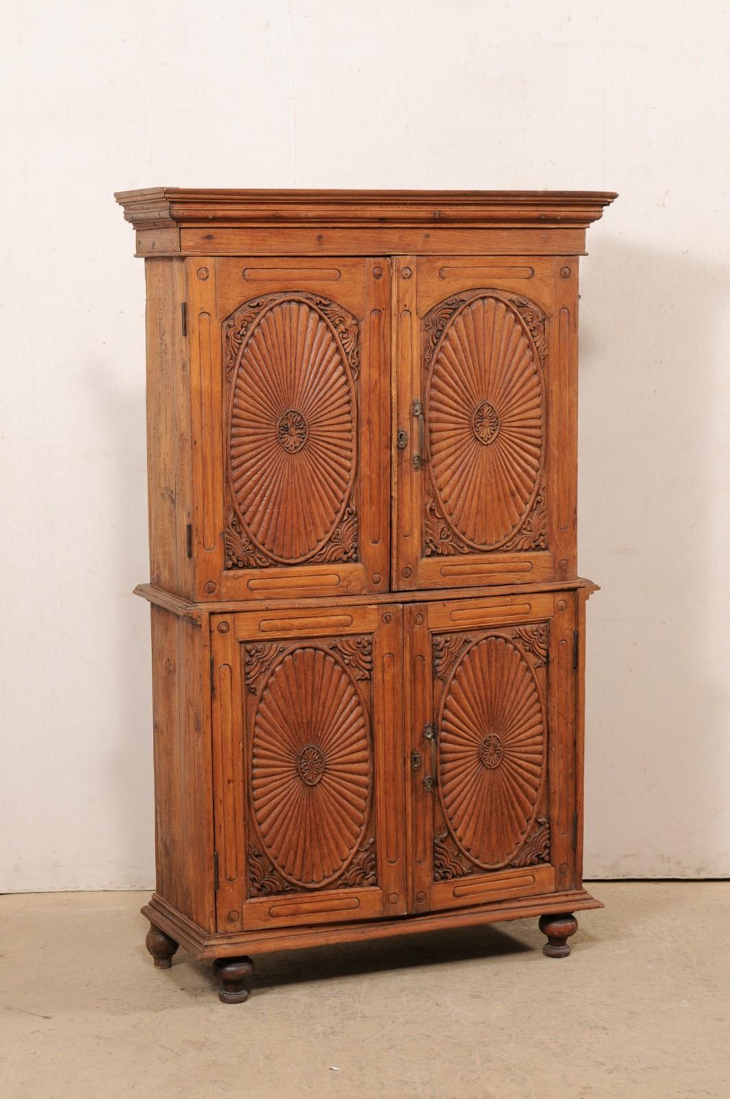 A tall British Colonial carved-teak wood cabinet from the 19th century. This pair of antique Anglo-Indian cabinets each feature a nicely molded cornice atop two stacked-pair of beautifully-carved, raised panel doors (four doors in total), which open