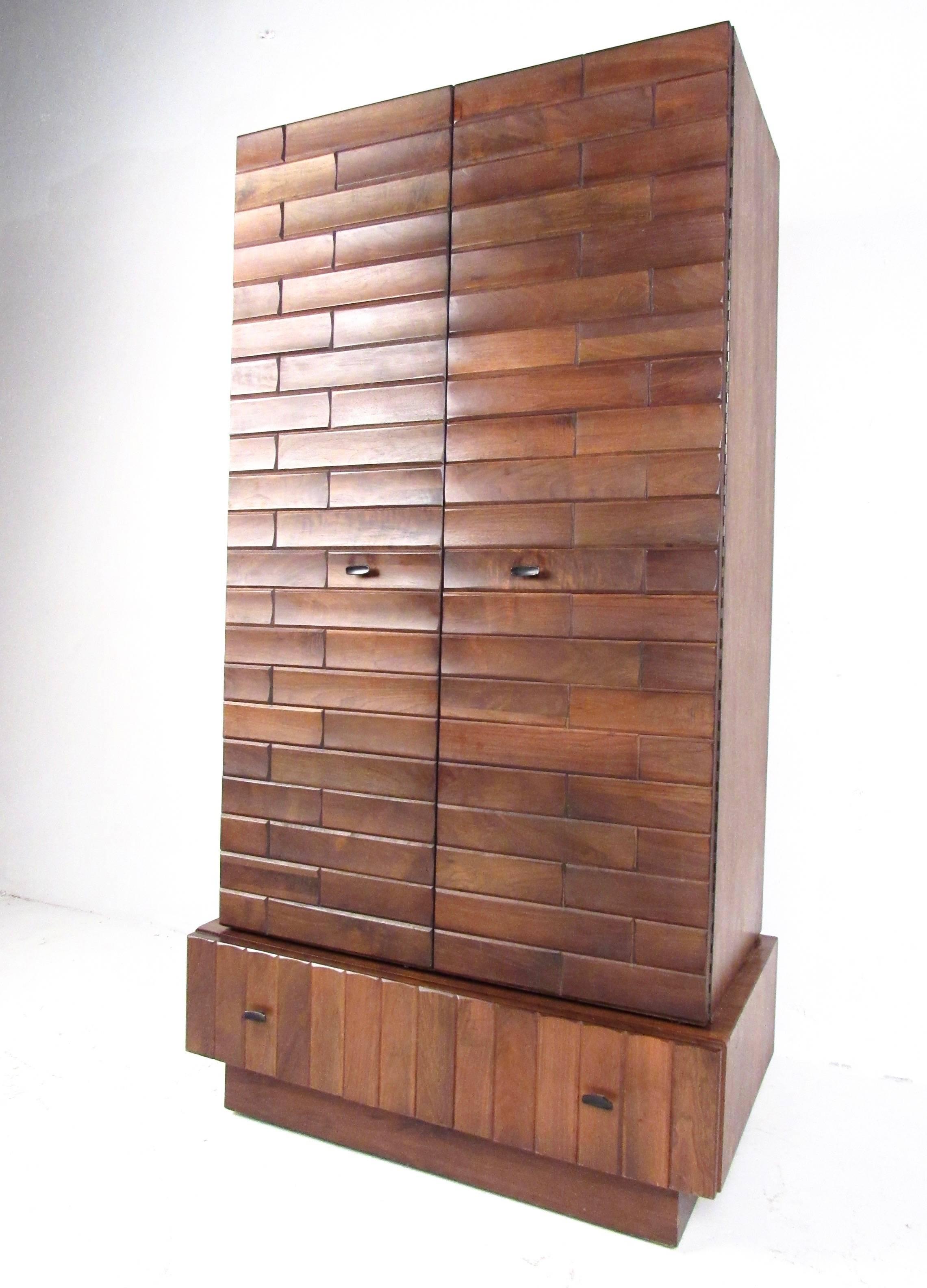 This stylish large-scale armoire features vintage walnut finish, sculpted Brutalist style fronts, and spacious interior cabinet perfect for bedroom storage. Metal drawer/door pulls add to the appeal of this uniquely tall midcentury two-piece cabinet