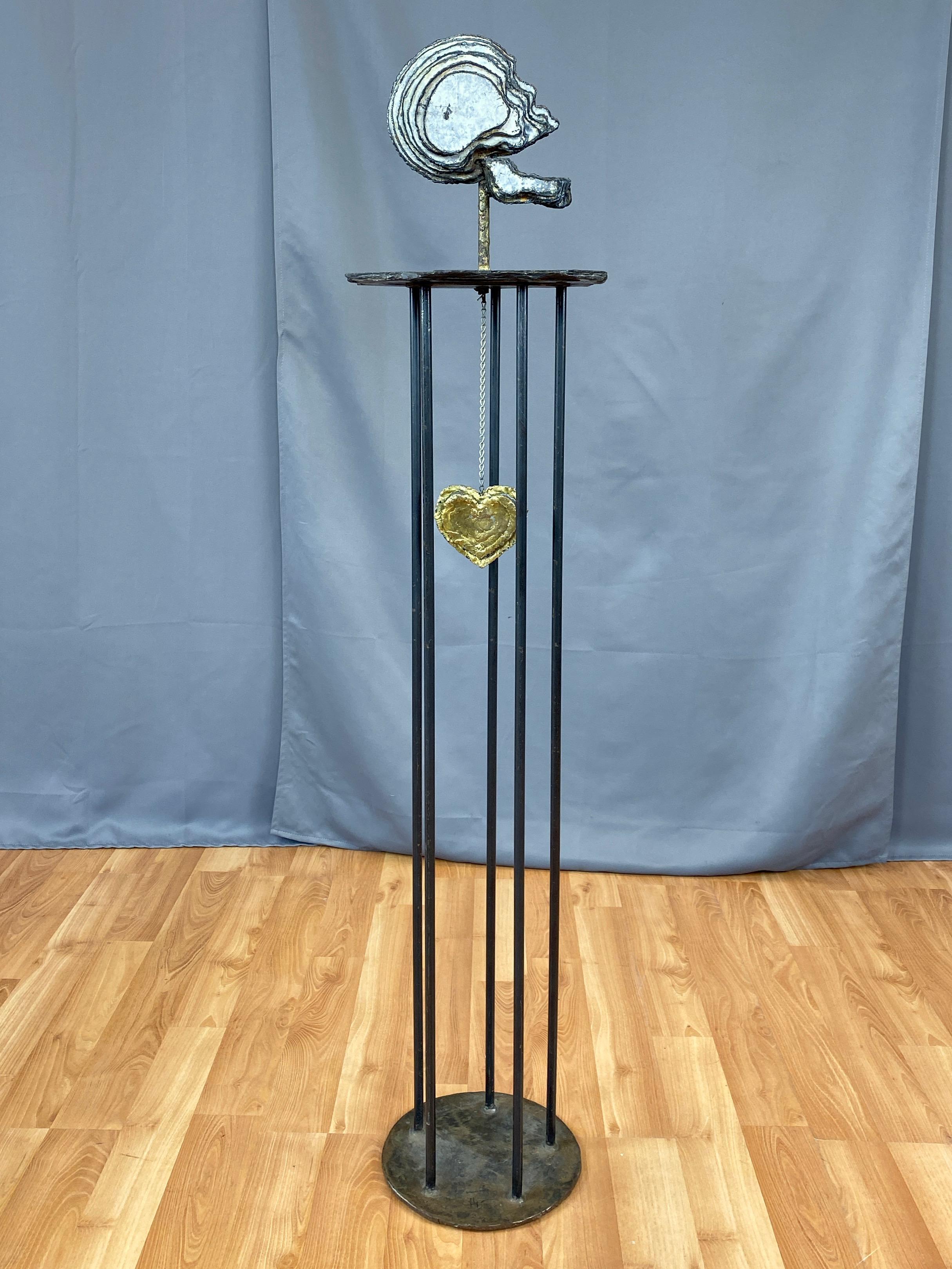 A 1990s custom commissioned steel, brass, and slate tall Brutalist skull and heart sculpture.

