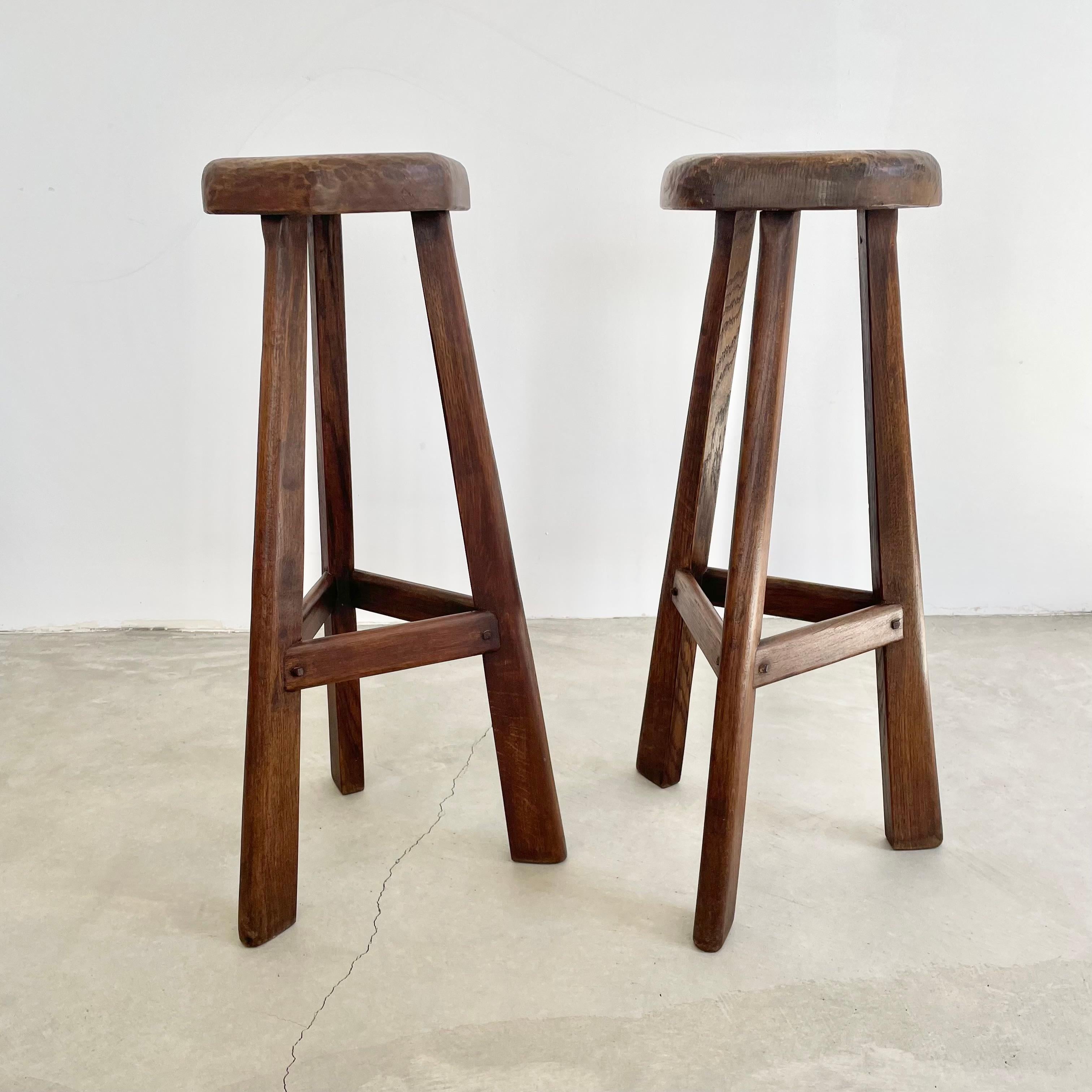 Beautiful brutalist tripod stools made in France, circa 1960s. Substantial and chunky triangular seat with rounded edges. Chunky legs that taper towards the top and have wooden crossbars 3/4 down the length of the legs fastened with wooden pins.