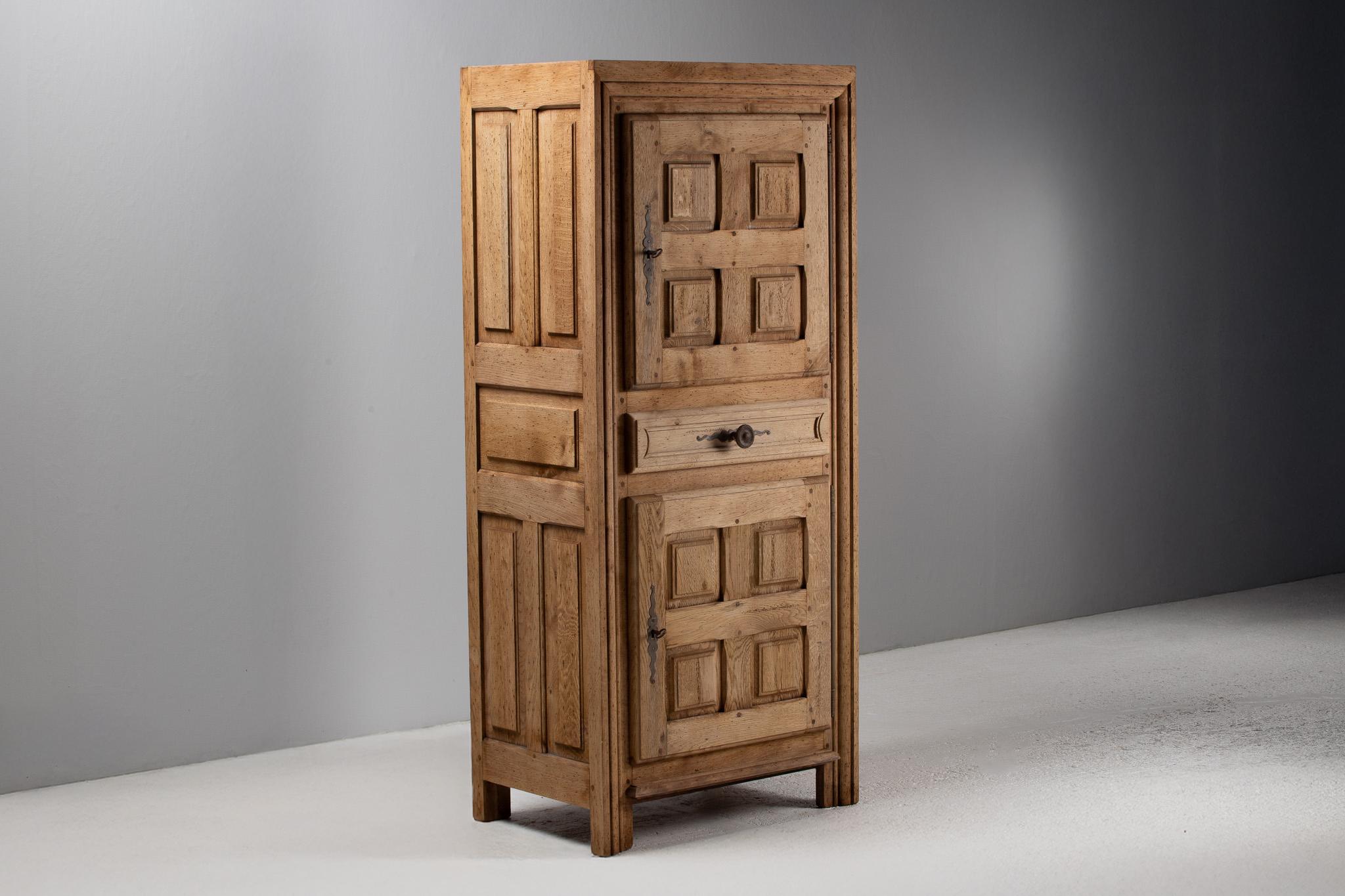 Solemn in bearing yet tactile in its detail, this tall cabinet stands like a monolith of rural memory—its verticality softened by the rhythmic repetition of recessed panels and timeworn grain. The façade is arranged in a tripartite structure: two