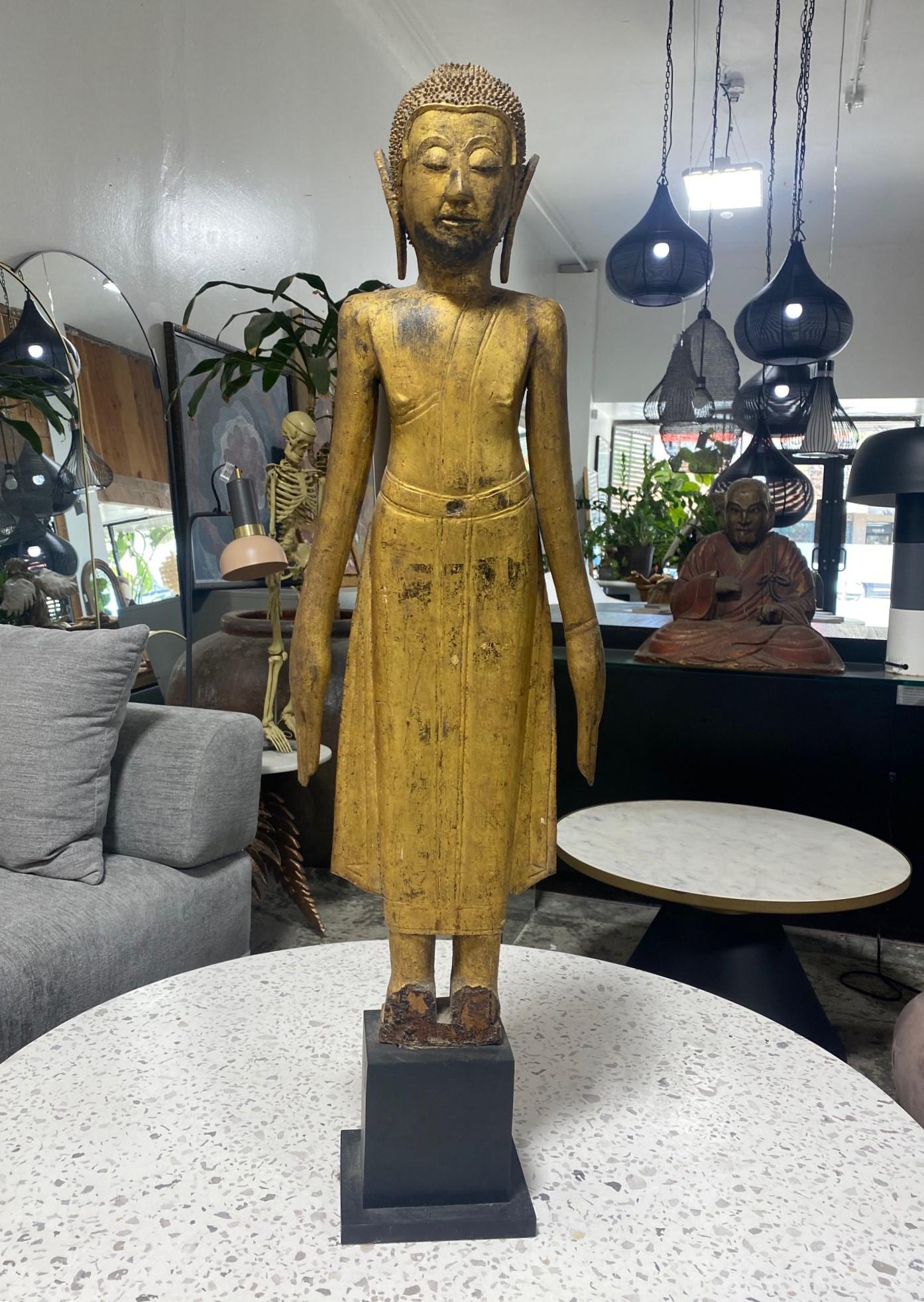 A well-carved and detailed carved wood temple shrine standing Buddha on a custom display stand. Decorated with golden gilt.  Likely Northern Thai or lower Burma/Burmese. 

This particular Buddha has a wonderful serene expression.

Was part of a