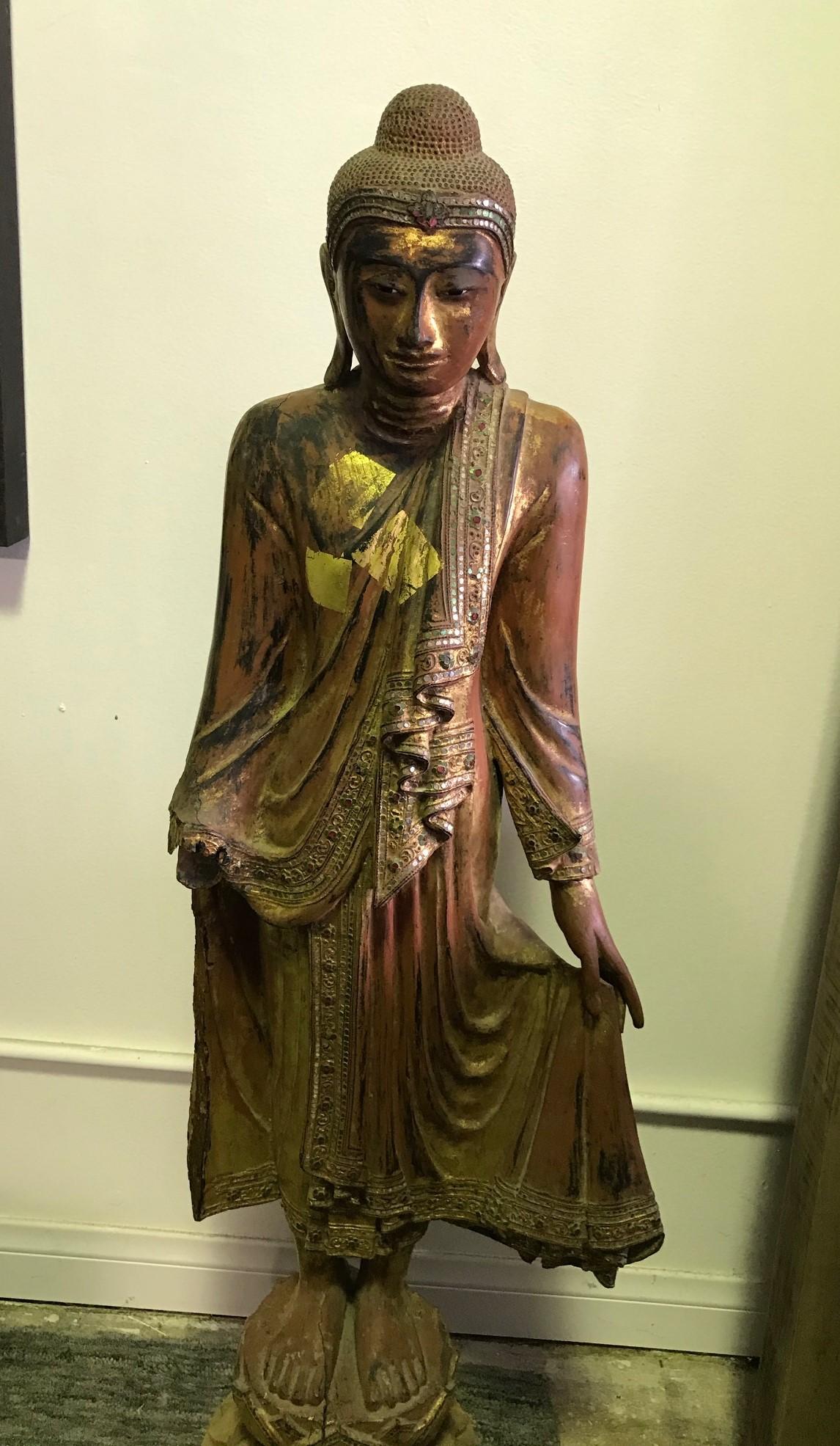 Tall hand-carved wooden standing Buddha. Beautifully carved and finely detailed. Likely Thai or Burmese. Decorated with lacquer and gilt (please see the gilt offering patches. Very unique and somewhat hard to come by). 

Would be a great addition