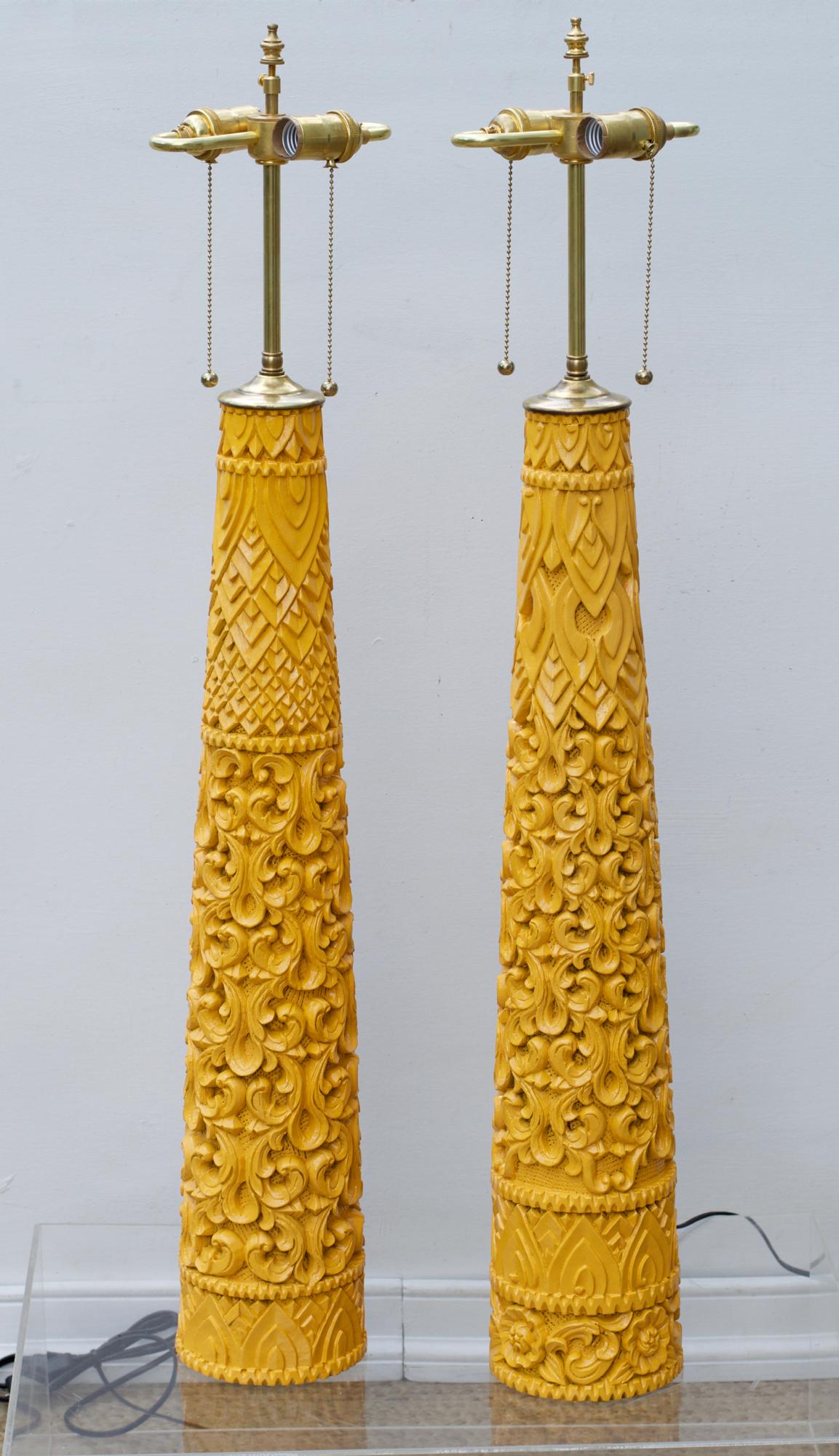 A near pair of slender and tapering carved wood lamps in an electrifying marigold yellow spray. The 1970s vintage cylinders are most likely Indian and will bring the Boho / Global vibe to any space in which they are employed.