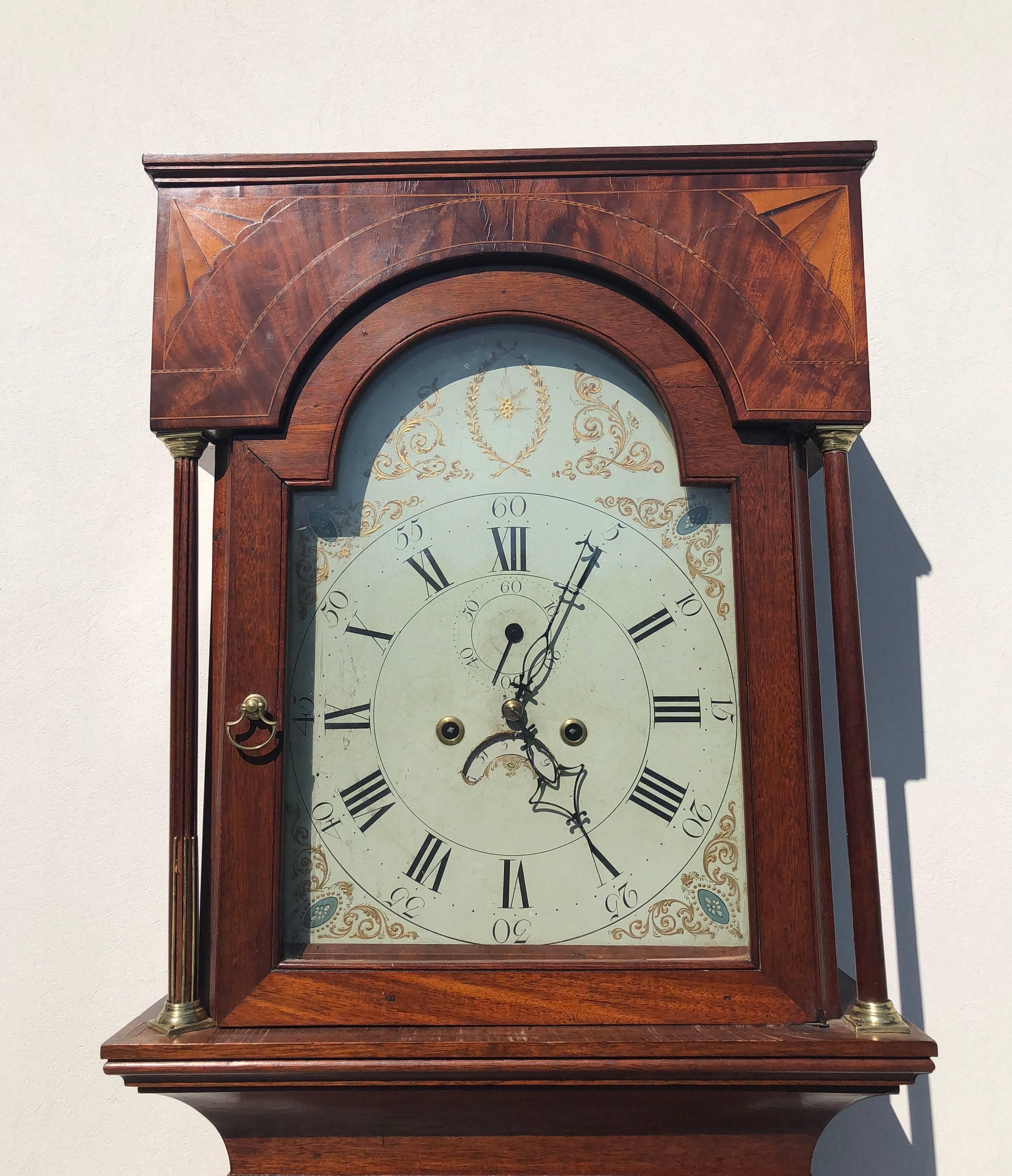 Stately English Hepplewhite period Grandfather clock with original works and enameled Dial. The mahogany case stands on Hepplewhite feet, has quarter fluted and reeded columns with brass accents and gorgeous fan inlays on the top of the rectangular