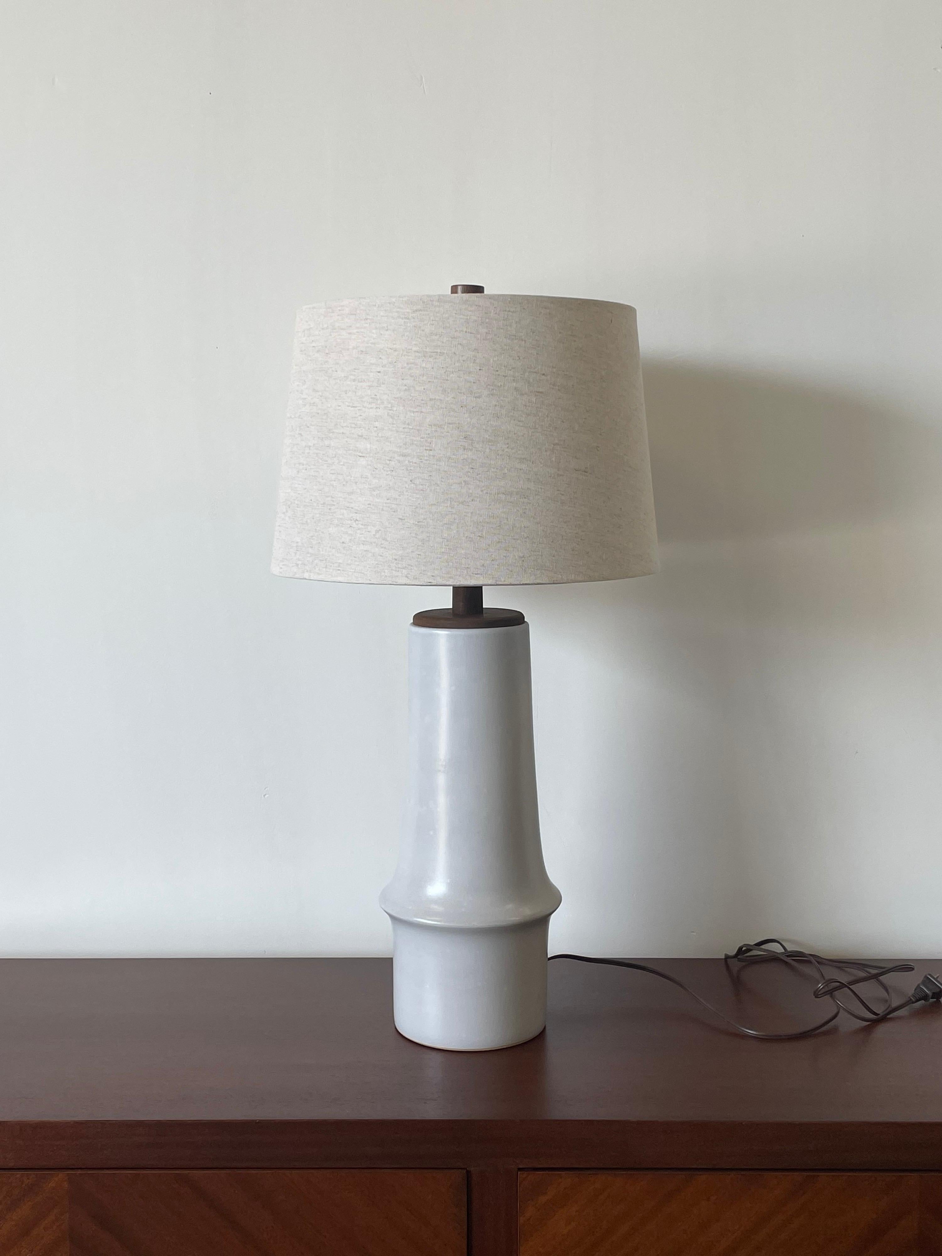 A large and elegant table lamp designed by famed ceramicist duo Jane and Gordon Martz for Marshall Studios. Lamp consists of a tall ceramic off white body with walnut disk, walnut neck, and finial.

Measures: Overall 
 29”