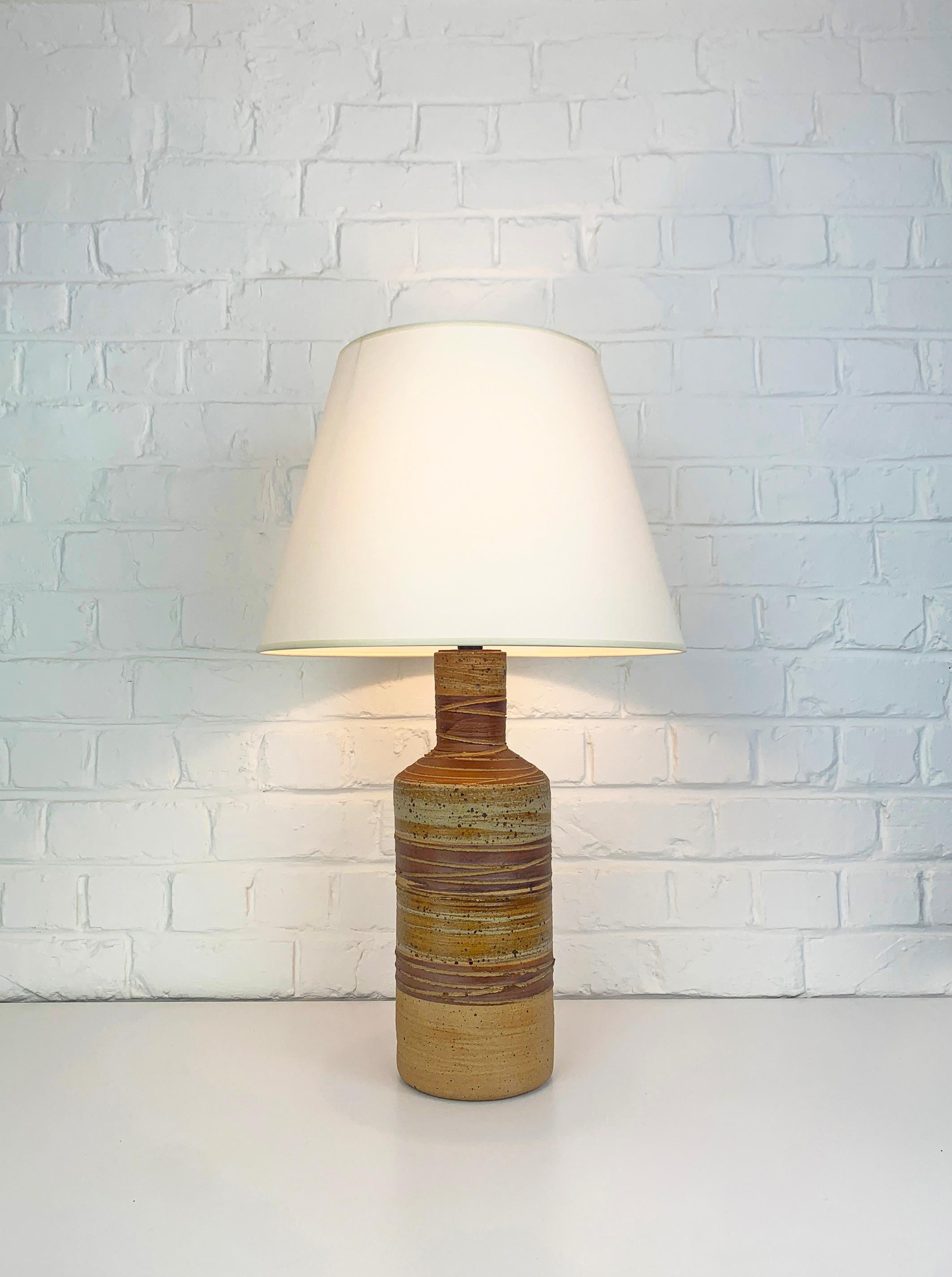 Lampe de table rustique créée par Tue Poulsen (Danemark). Fabriqué dans les années 1970-80 dans le propre Studio de Tue Poulsen.

Le pied de la lampe est en terre chamottée et décoré de rayures dans les couleurs de terre brun-beige. L'argile
