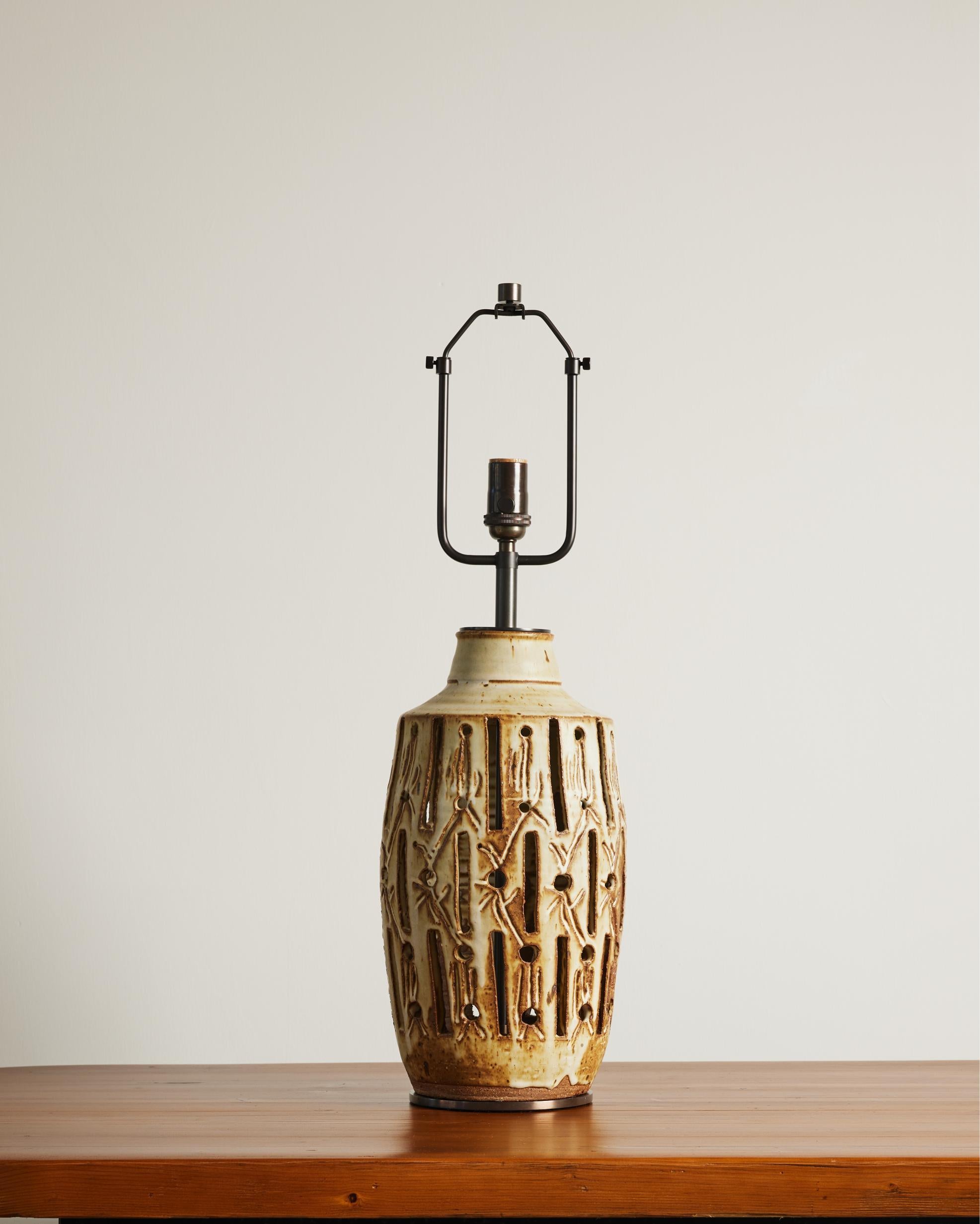 Tall and distinct table lamp made of glazed ceramic, with incised motifs and a patinated bronze base.

The lamp features an adjustable harp, with the overall height ranging from 26 to 30.25 inches.
This piece is newly rewired with an 8-foot black
