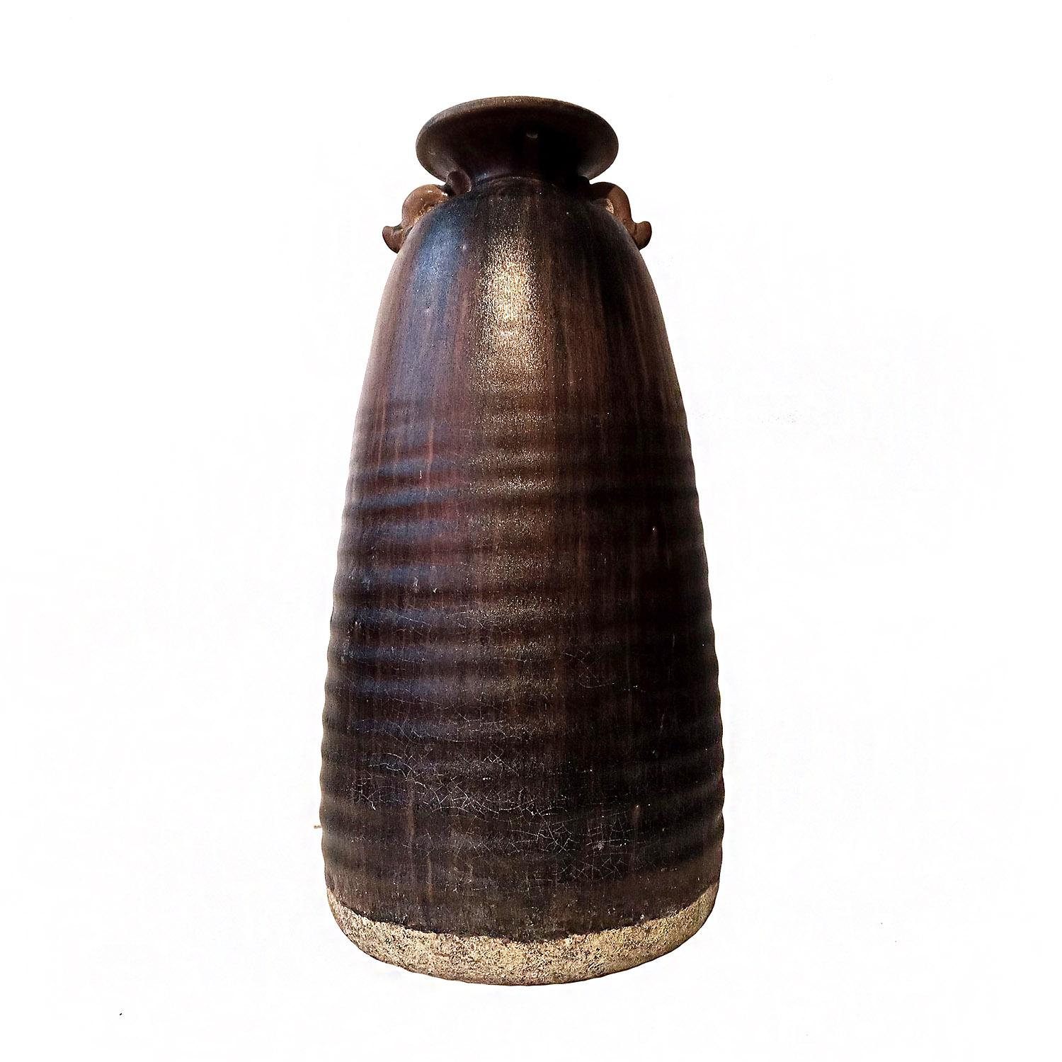 A tall brown ceramic vase / urn with dark brown glaze, with small ears on its neck. Hand-crafted in Thailand, in the tradition of antique Thai earthenware. With its ribbed texture and mottled brown glaze, this piece makes for a unique decorative