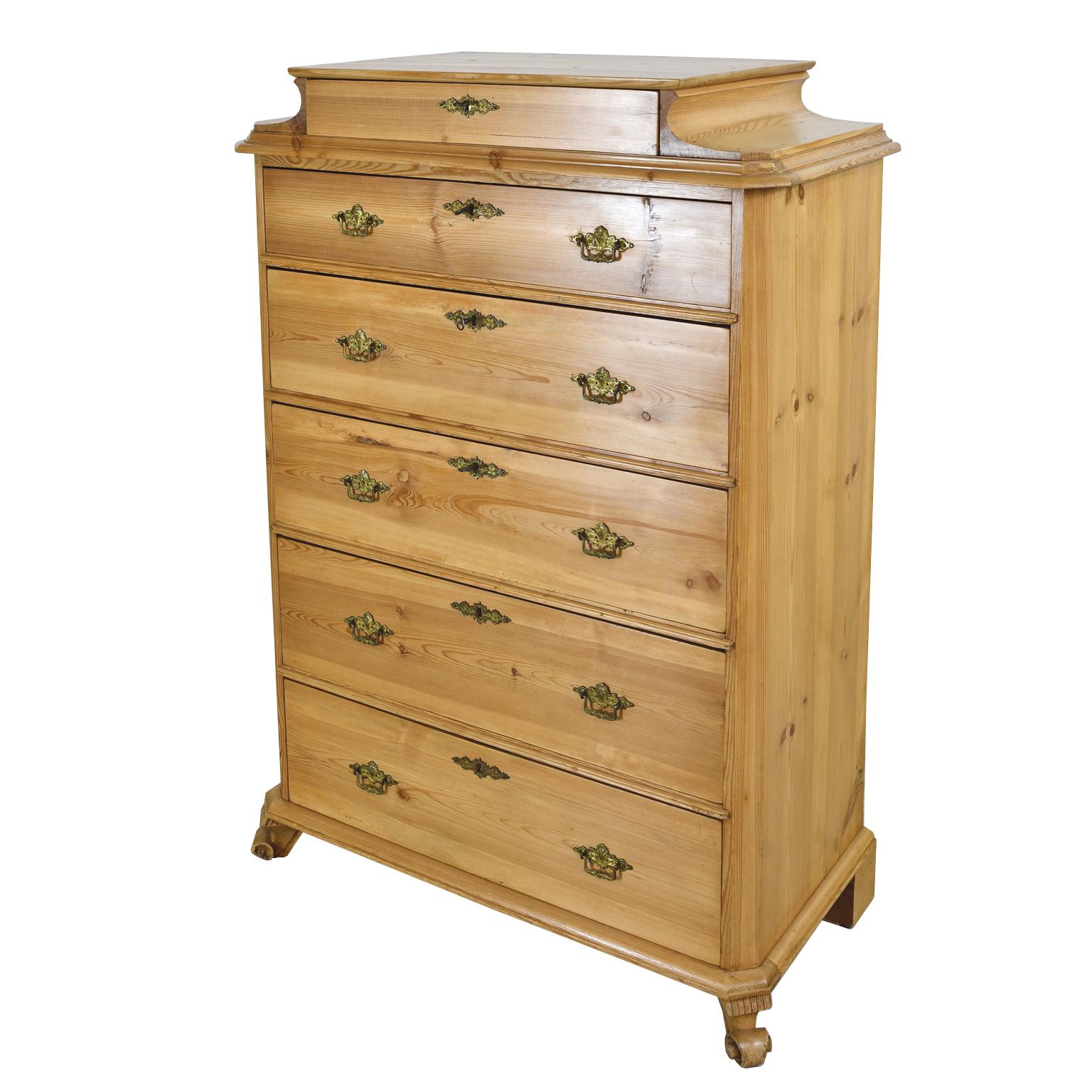 A charming chest in pine that is beautifully designed and handcrafted with pedestal top offering one drawer followed by five larger drawers, all with original brass key plates and bales. Chest has chamfered corners and rests on carved scroll feet.