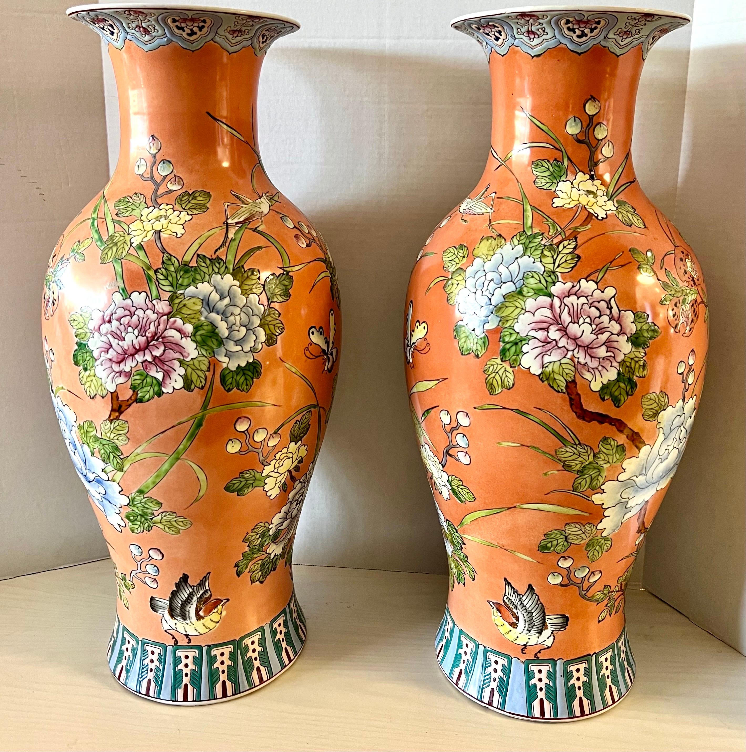 Very tall Chinese porcelain baluster form vases hand painted in the famille rose pattern on an orange ground with birds in flight and grasshoppers over blossoming chrysanthemum, pomegranates and other flaura.