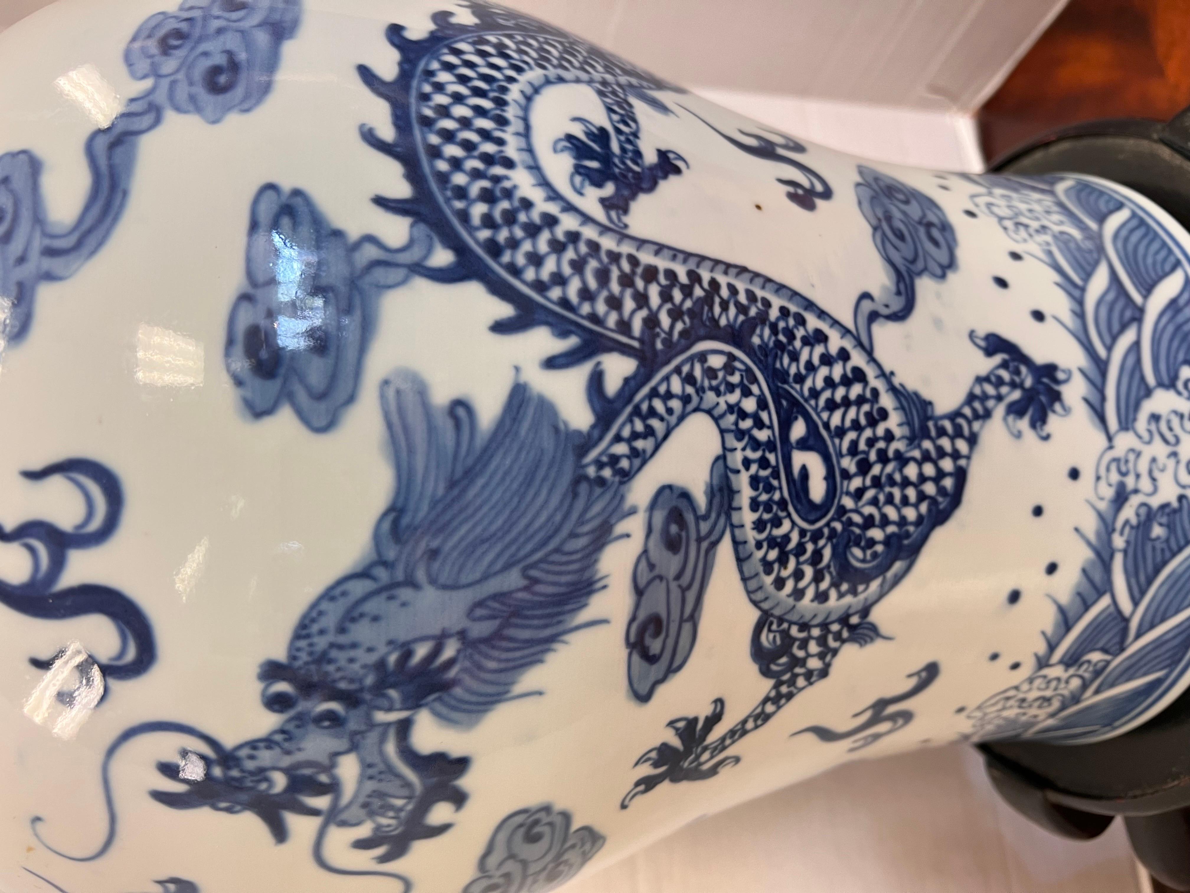 Chinese blue and white covered urn features a dragon motif on front and back.  Displayed on a carved wood pedestal.  No hallmarks and there is a flaw we have photographed.