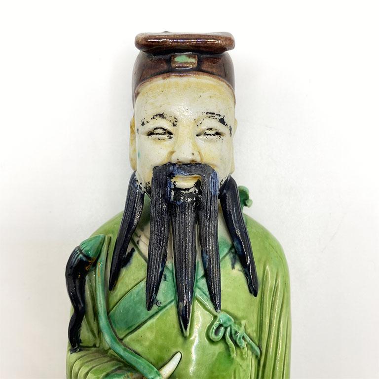 A superb example of Chinese artwork, this ceramic figurine will look stunning on a bookshelf. The man depicted stands upon a rectangular emerald green box. He wears a robe in a lighter shade of green. He wears a dark brown traditional headpiece and