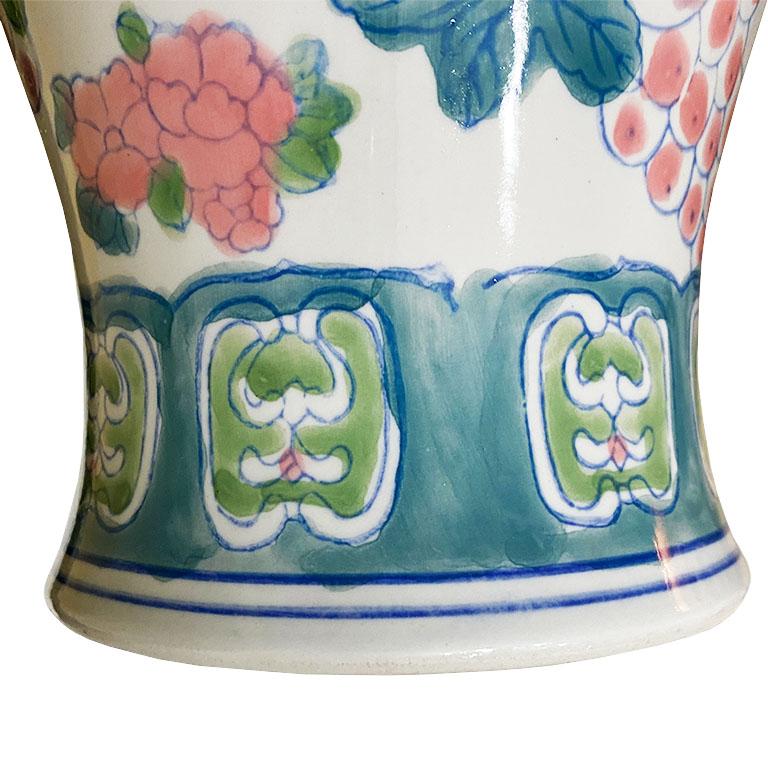 Dress up any table with this tall beautiful chinoiserie vase. A floral motif is glazed onto a white background. A green and blue stylized design decorates the round bottom. The body of the vase is decorated with pink lotus blossoms, berries, and