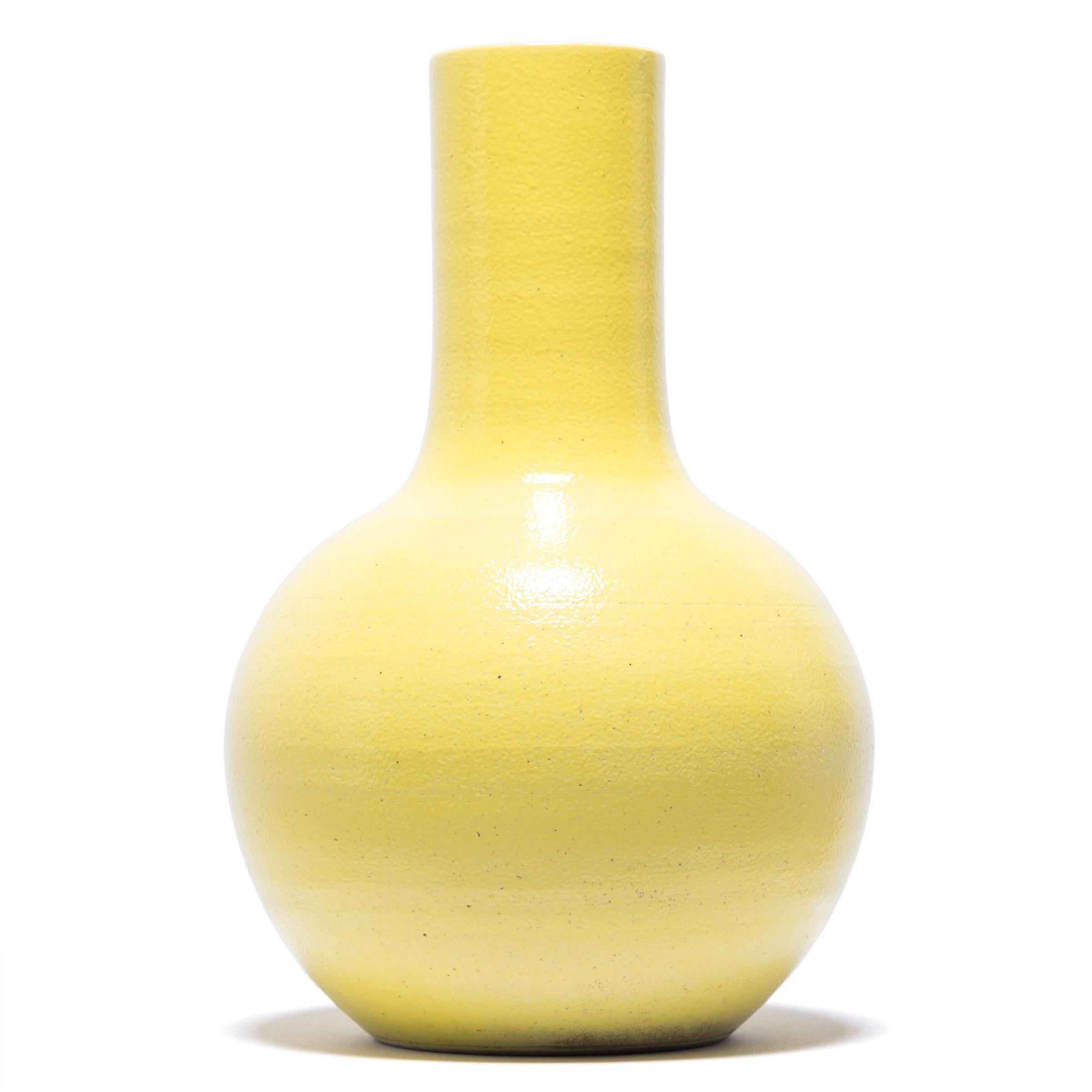Drawing on a long Chinese tradition of monochrome ceramics, this tall gooseneck vase is glazed in cheerful citron-yellow glaze. The vase features a rounded, globular body and a narrow cylindrical neck, a classic form known as 'tianqiuping' or