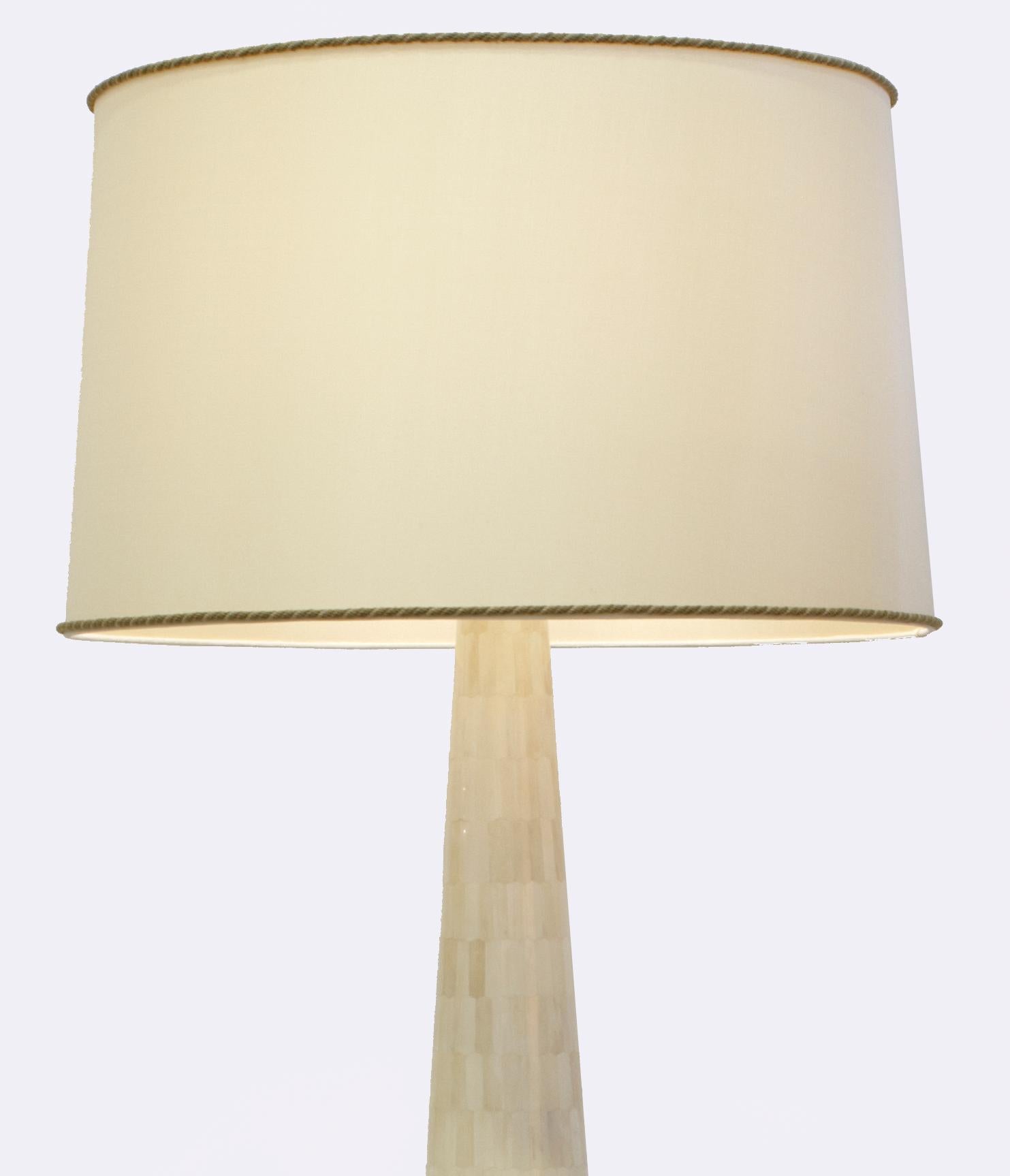 La lámpara de pie redonda Nima destaca por su elevada base cónica de madera maciza y su intrincado diseño de marquetería de hueso. La luz ilumina cientos de astillas cremosas de hueso de camello, creando un resplandor suave y cálido.
Pantalla de
