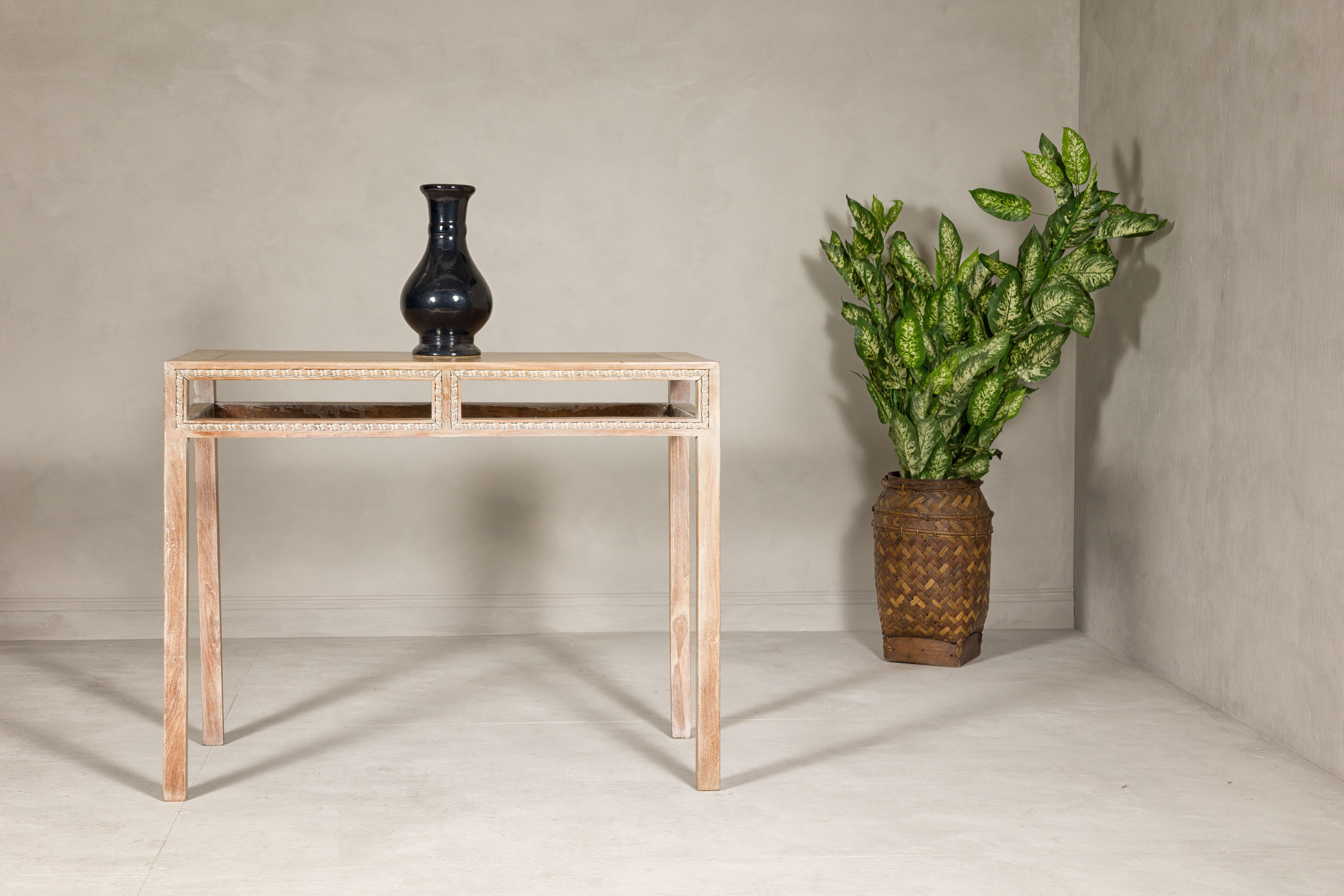 A tall wooden console table with carved beaded rope molding, whitewash natural finish, straight legs and open apron. This vintage console table, standing tall with its gracefully straight legs, embodies a refined simplicity complemented by a touch