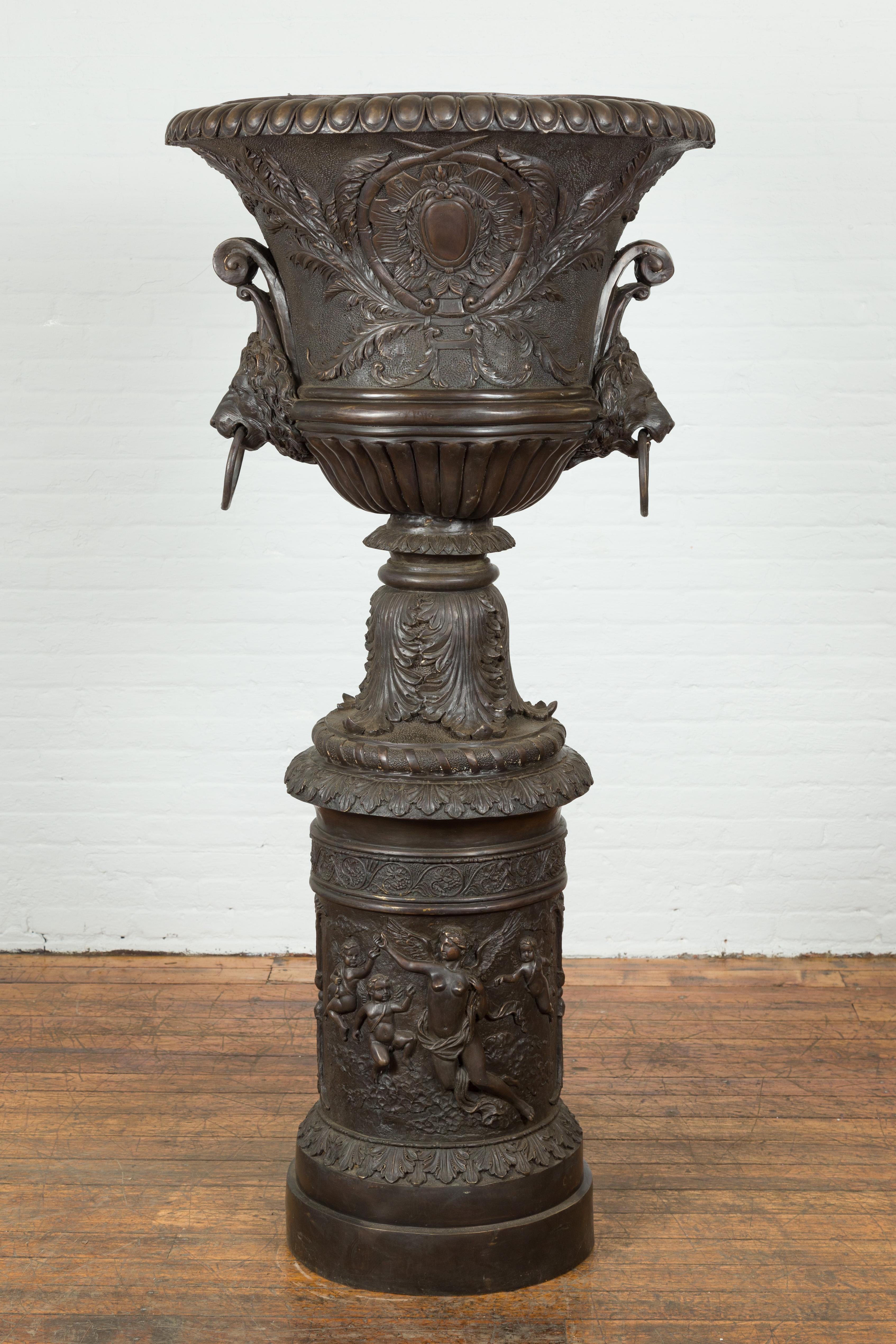 A custom made tall and large lost wax cast bronze urn on pedestal adorned with lion head handles. Created with the traditional technique of the lost-wax (à la cire perdue) that allows a great precision and finesse in the details, this bronze urn