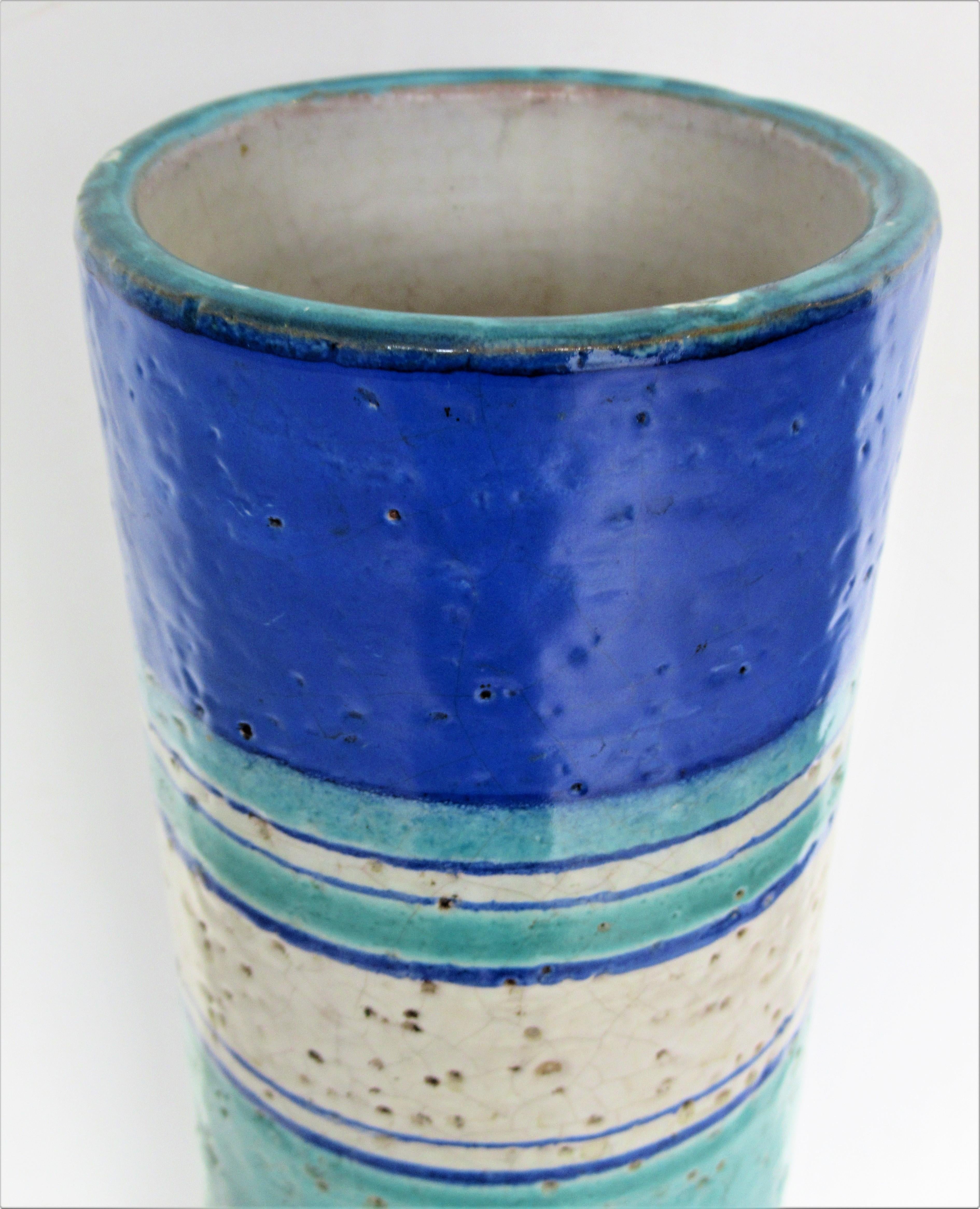 A tall cylinder shaped ceramic vase by Bitossi with beautifully textured surface and brilliant glazes of turquoise, cobalt blue, ivory in an alternating concentric ring design. Circa 1960.  Signed on underside Italy 4733. Measures 17 inches tall.