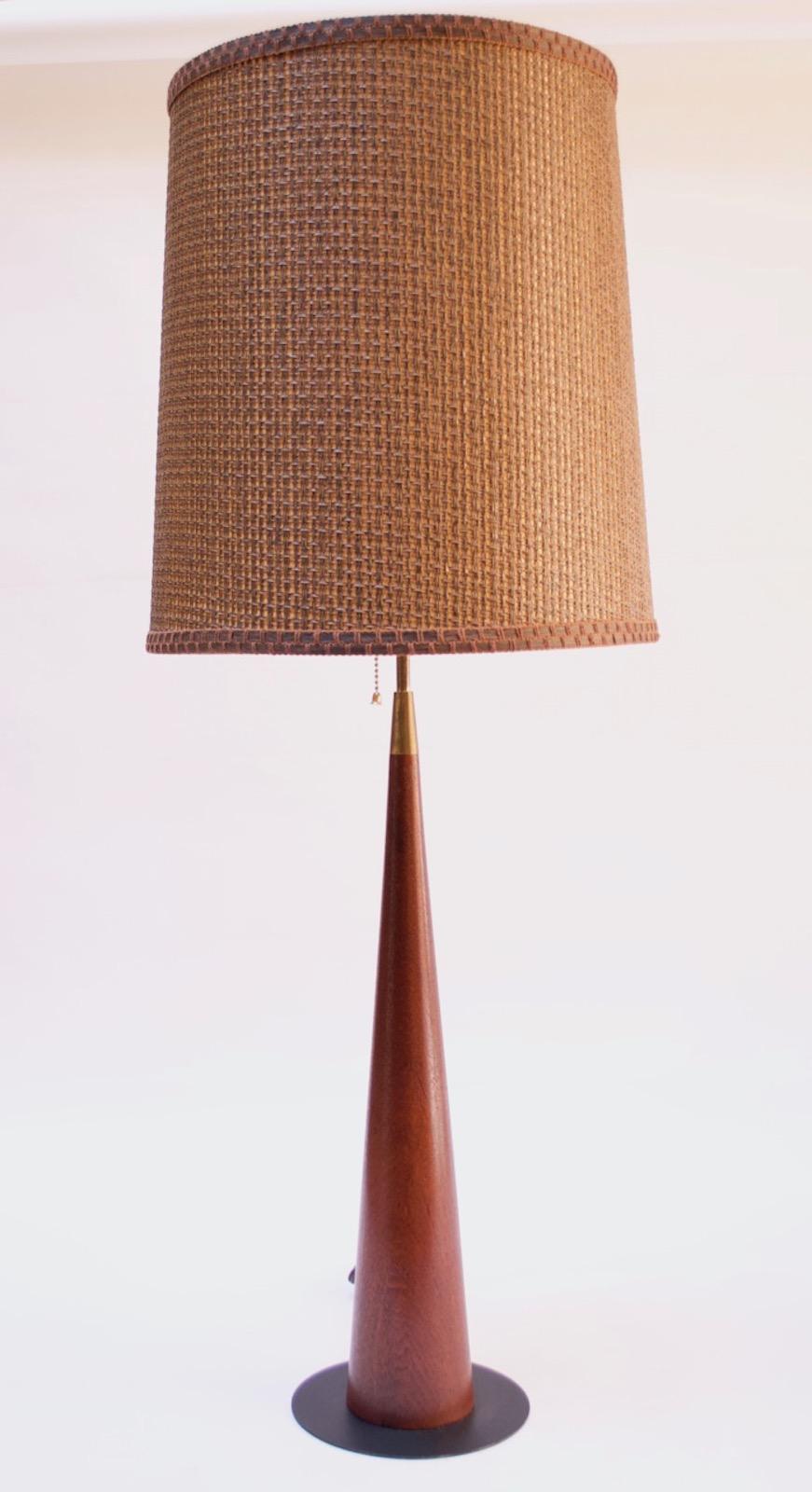 Cette lampe de table danoise des années 1960 est élégante dans sa simplicité. Elle est composée d'un cadre conique en teck relié par un col/tige en laiton au sommet et d'une base circulaire en métal noir. La forme modeste et les lignes épurées sont