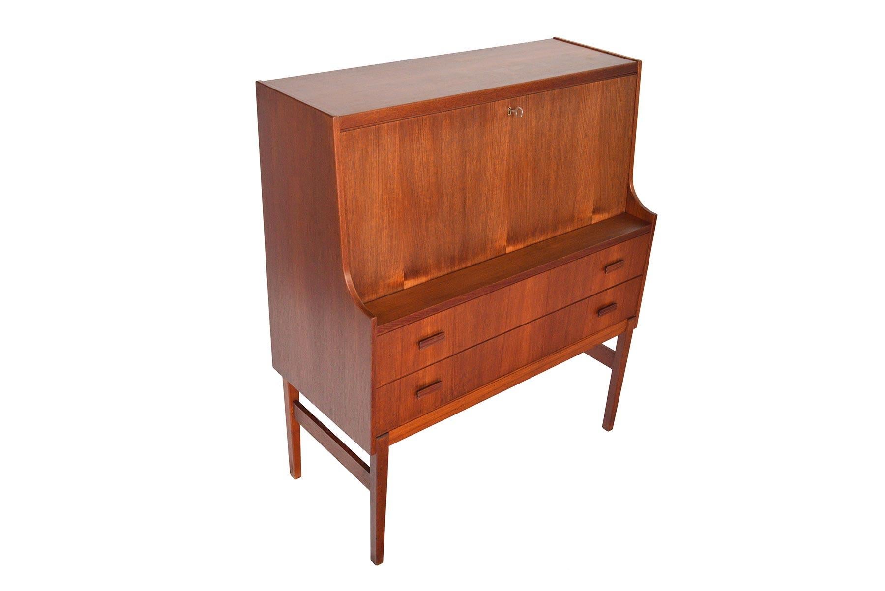 Offering complete concealed storage, this Danish modern drop front secretary desk is an excellent work space and storage piece. The large drop down desk surface reveals two cubbies behind sliding doors and a bank of three drawers. Two lower drawers
