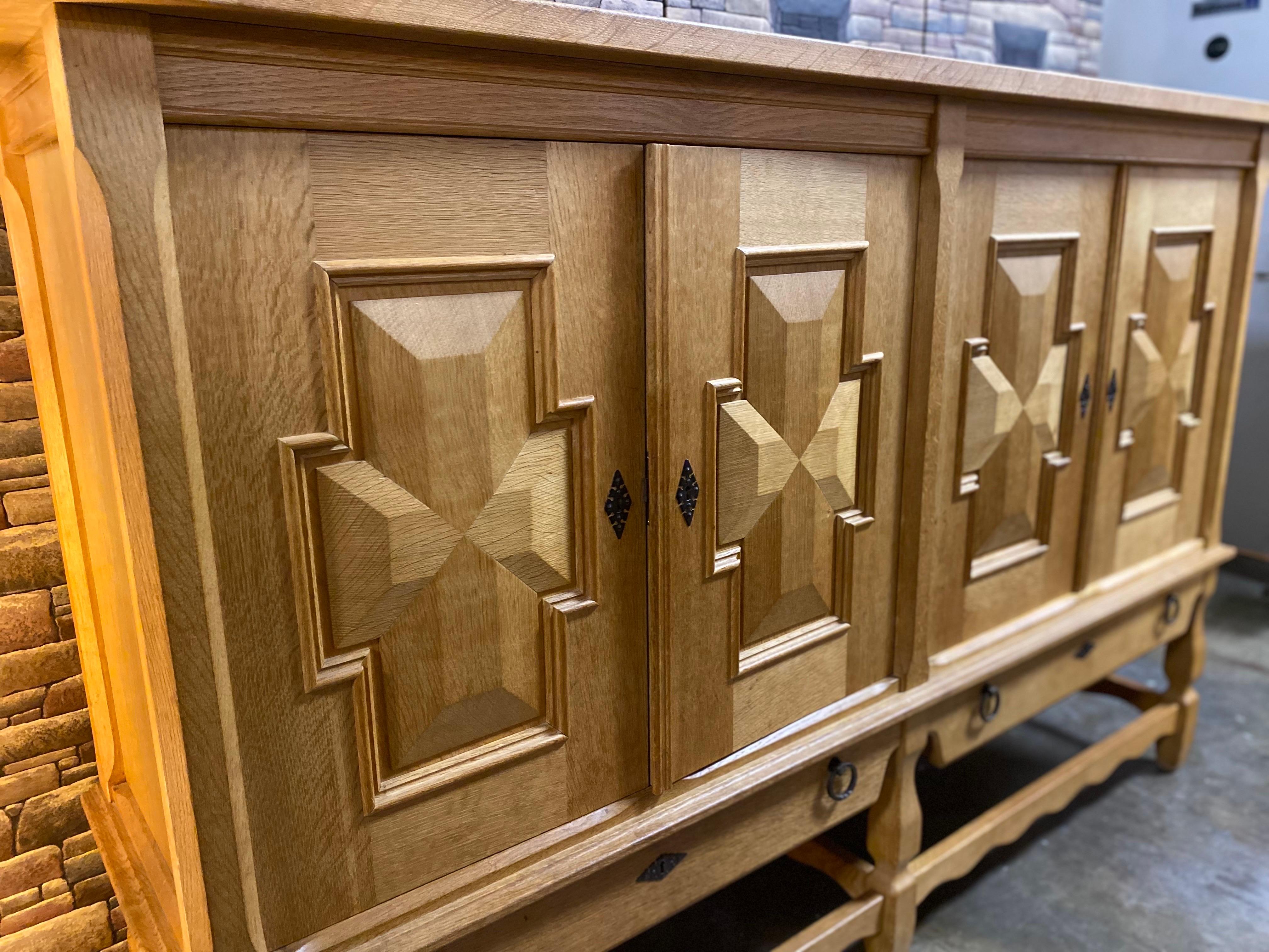 Henning Kjaernulf mid-century solid oak credenza. This Danish modern tall sideboard features four doors with carved accents opening to interior storage space featuring five shelves and three drawers, two lower drawers, on carved stretchered block