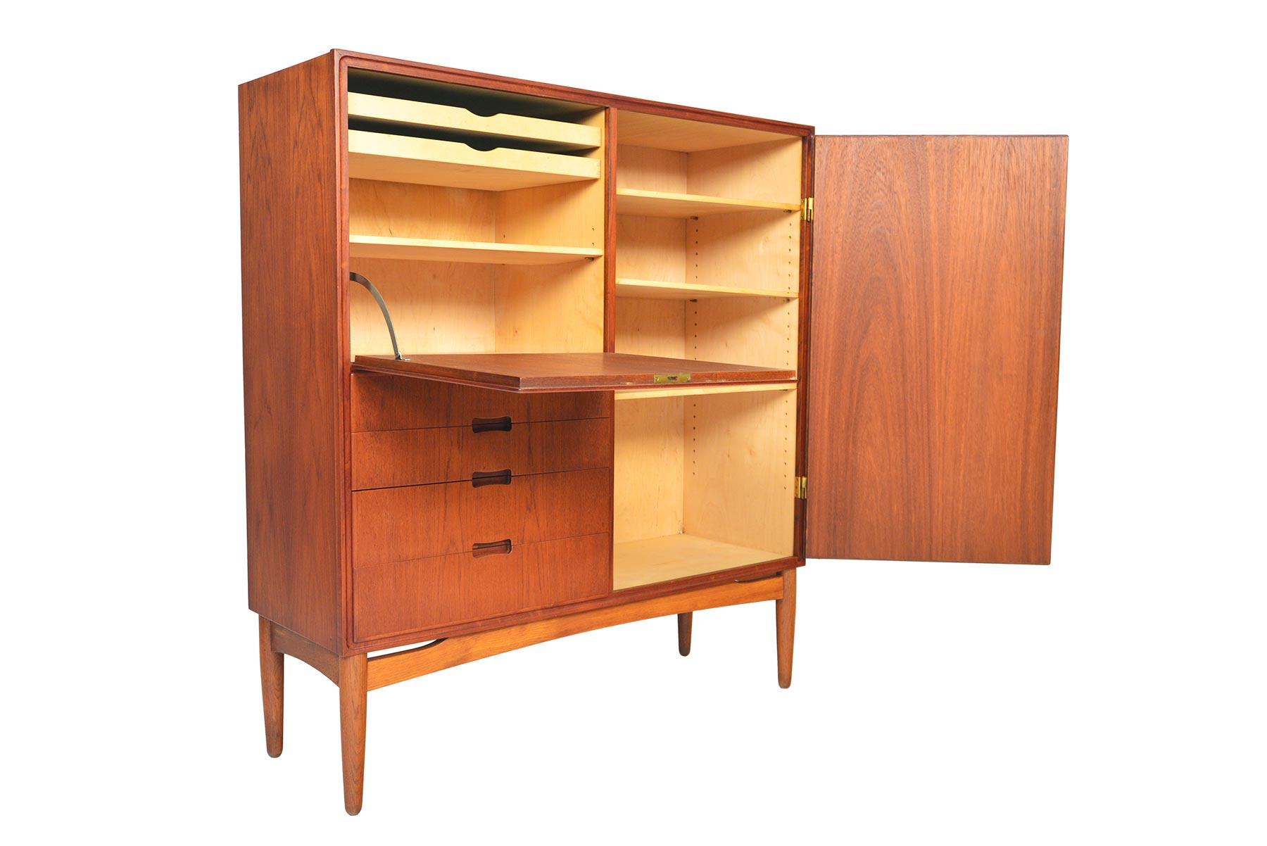 This tall Danish modern cupboard offers exceptional storage and design details. The left door is accessed by key and drops to reveal two drawers and adjustable shelving. A tall cabinet sits to the right of the case and is outfitted with adjustable
