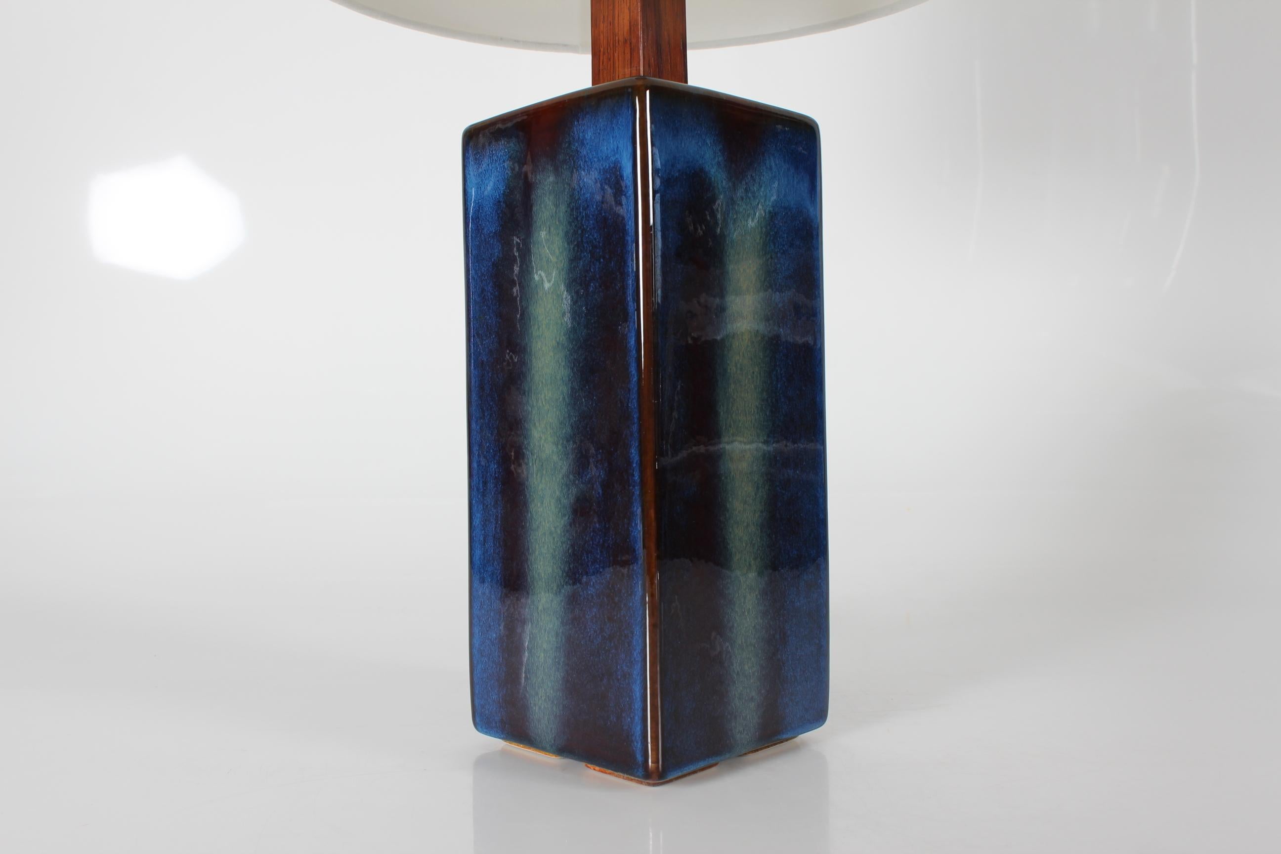 Tall sculpturel ceramic table lamp made by Søholm Stentøj, Denmark.
Made circa 1960s.

Decorated with midnight blue glaze with a twist of green turning into dark brown at the edges. 
The socket is fitted to a delicate square block of wood on top of