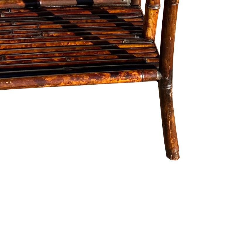 A beautiful chinoiserie standing magazine rack or sheet music stand. Lacquered pieces of bamboo are affixed together in an angled geometric design at the back of each rack. Four splayed legs with a bottom shelf are on the bottom. 
Brick caps are