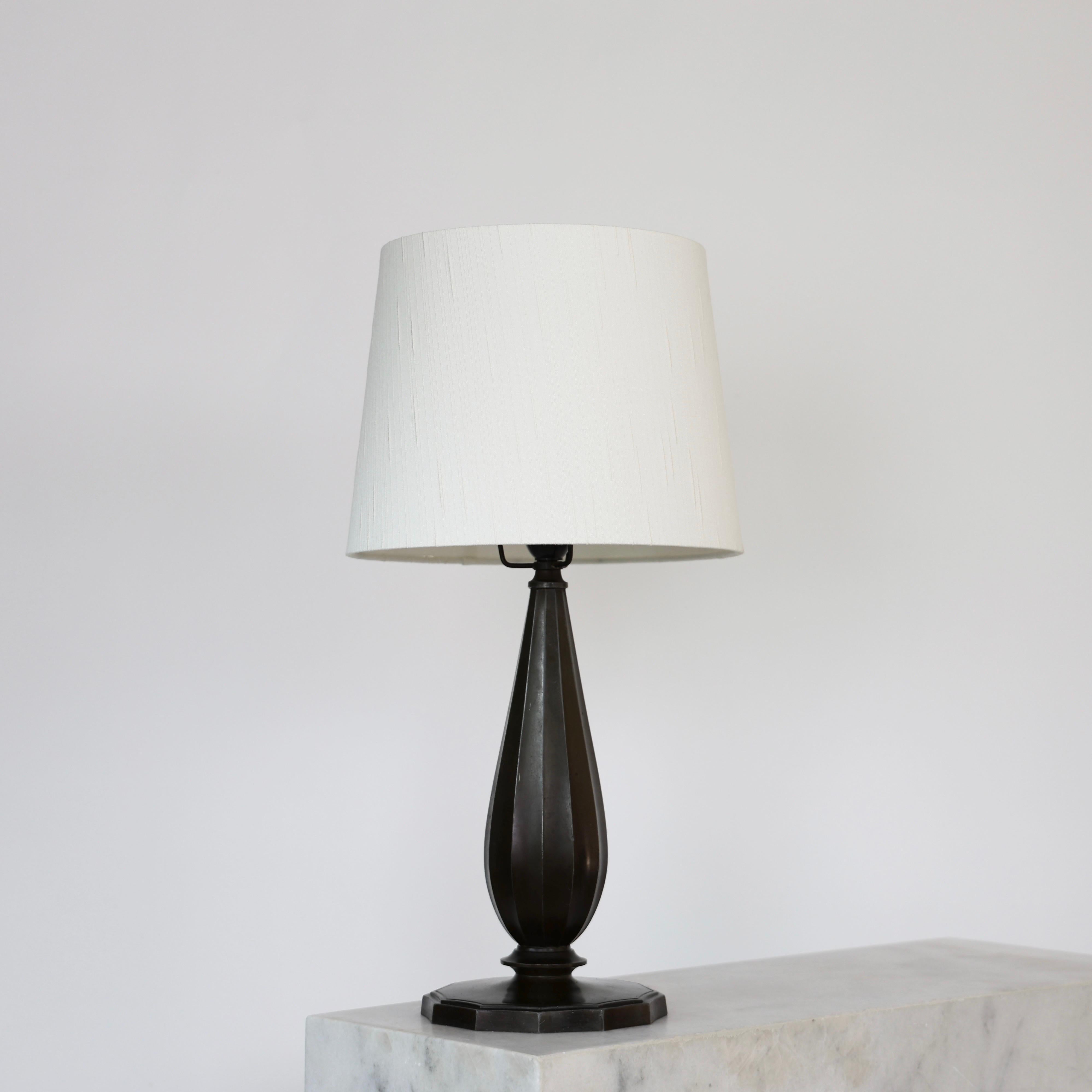 Grande lampe de table Diskometal conçue par Just Andersen en 1940. Une pièce élégante pour un lieu magnifique.

* Lampe de bureau diskometal en forme de bouteille avec des lignes verticales et un abat-jour en tissu blanc.
* Designer : Just