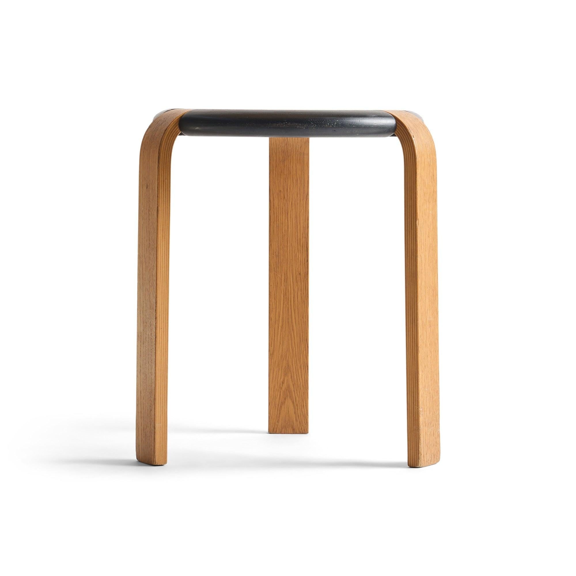 Uno sgabello con tre (3) gambe in laminato che si inseriscono in una seduta a ciambella ebanizzata in legno laminato sagomato.