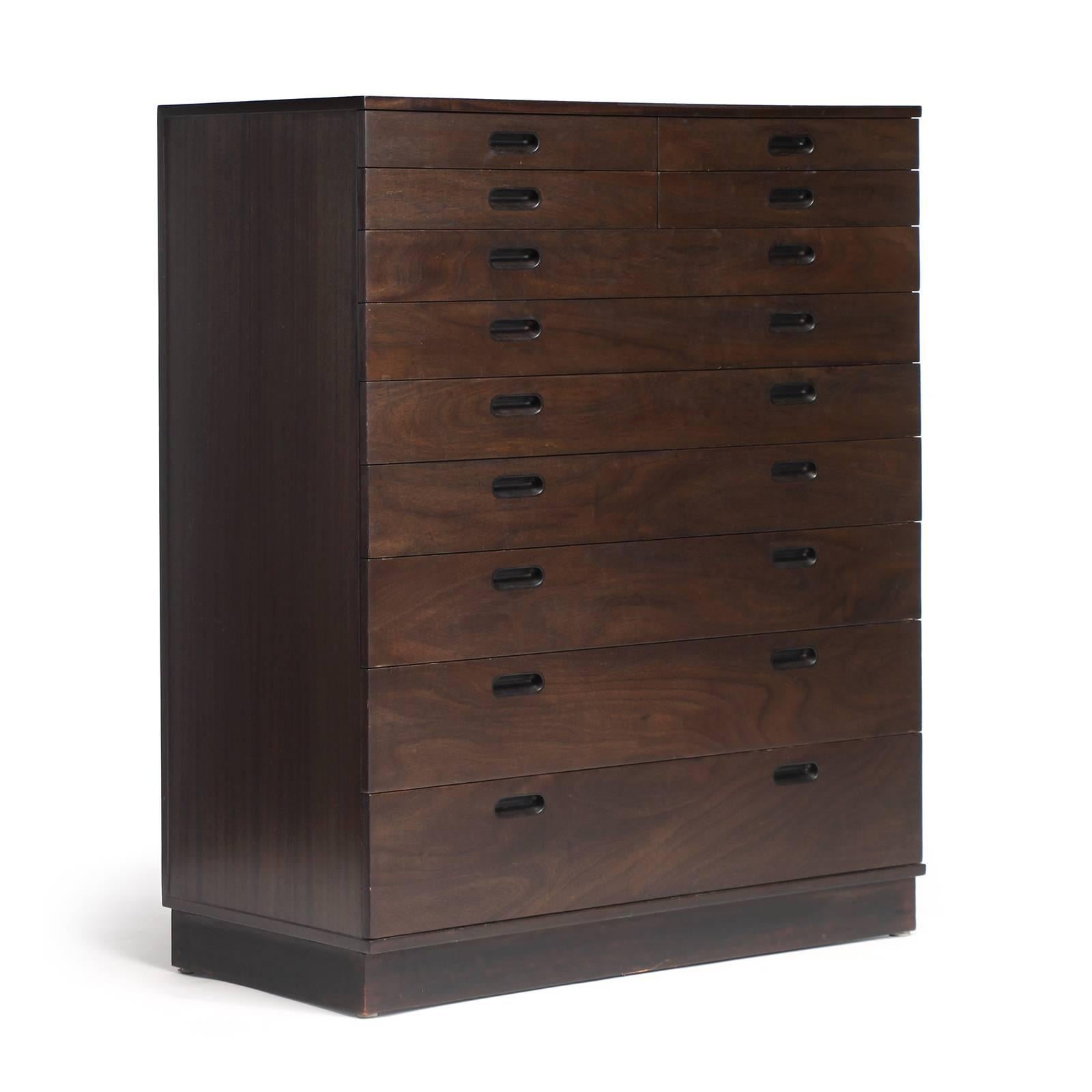 A tall rectilinear chest of eleven drawers in richly figured walnut having a four-over-seven-drawer configuration, a leather-wrapped plinth base and distinctive recessed pulls.