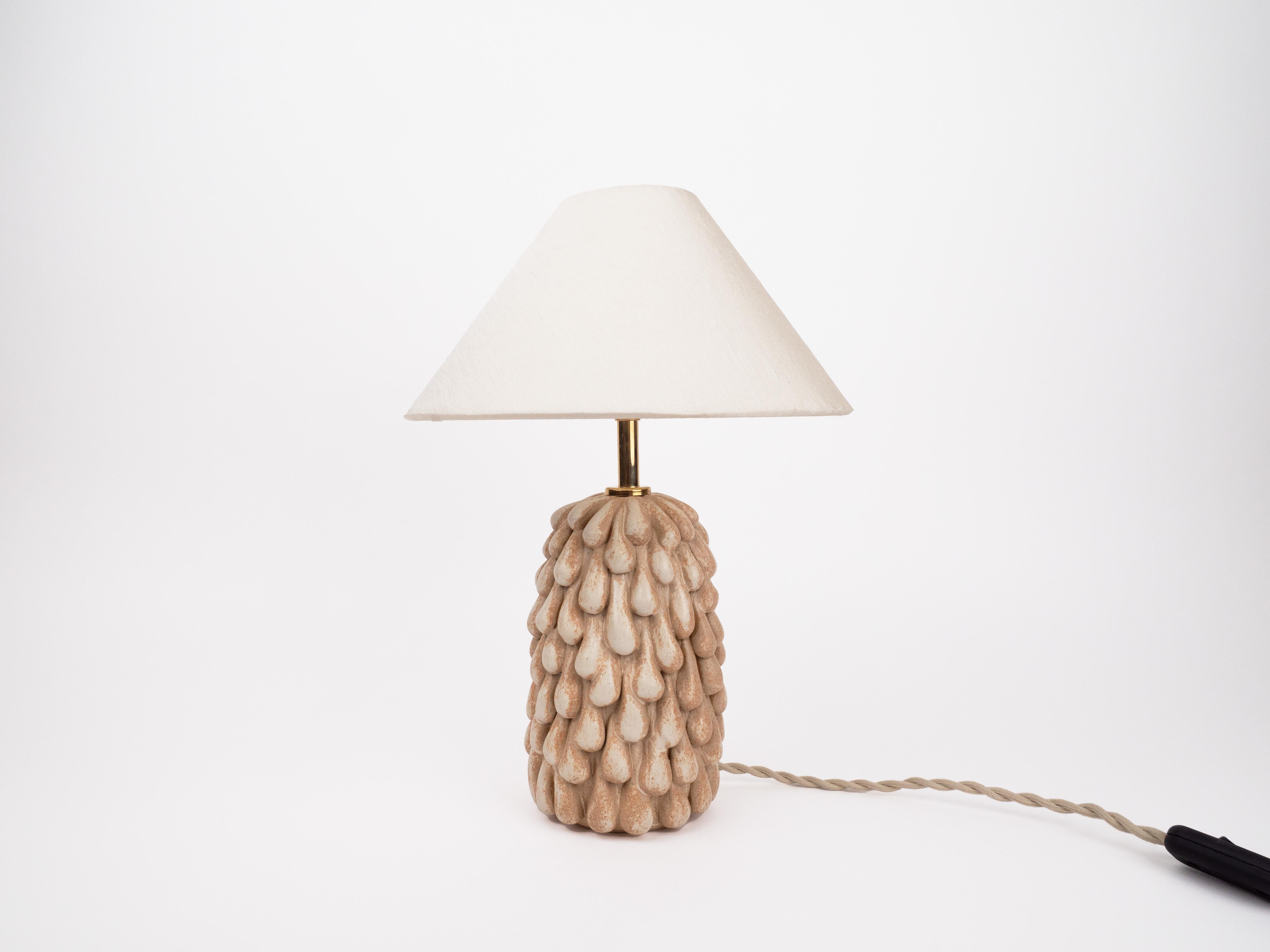 Ajoutez une touche d'élégance et d'art à votre intérieur avec cette superbe lampe en grès crème satiné. La finition lisse et satinée de la lampe dégage une sophistication intemporelle, tandis que la texture unique en forme de goutte ajoute un