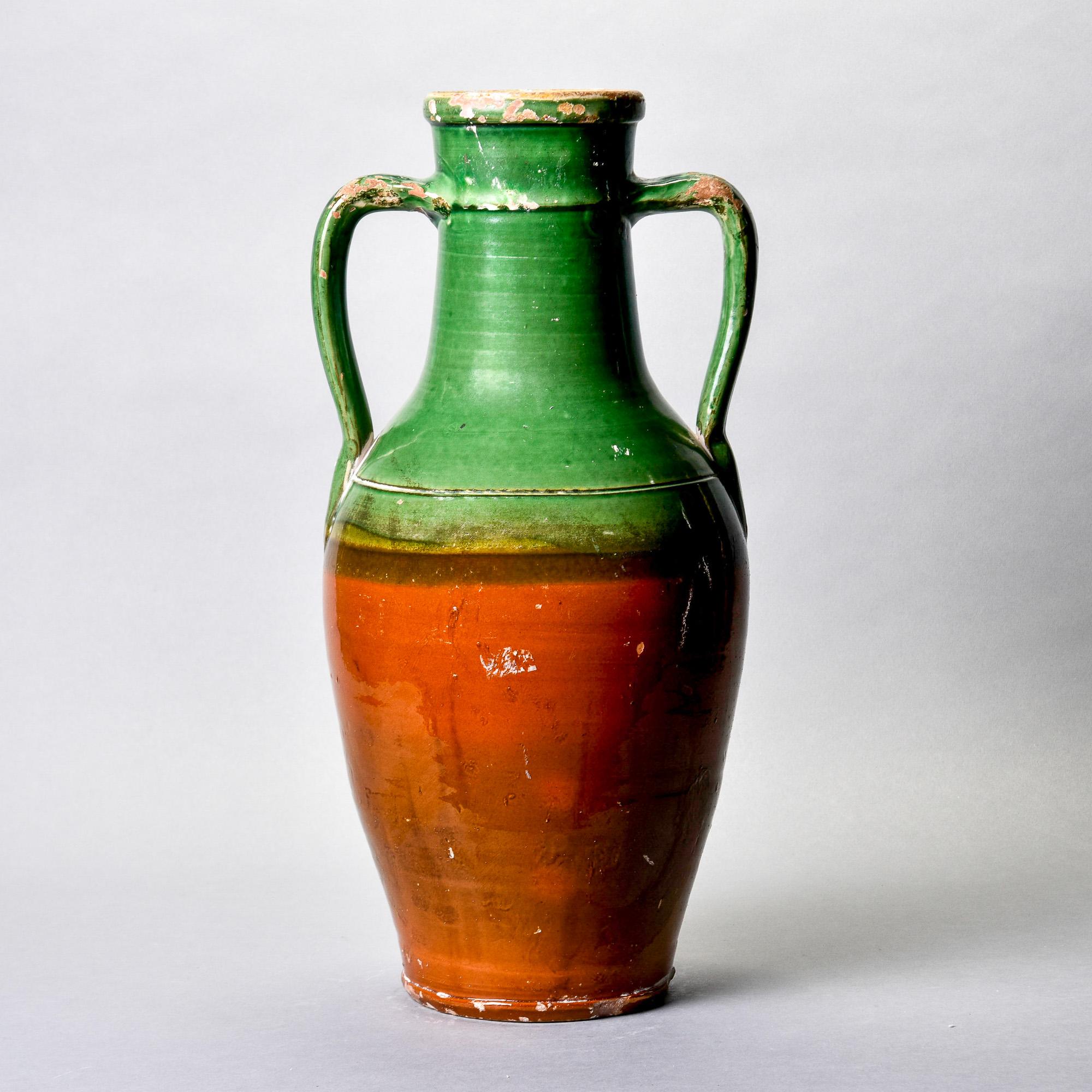 Found in France, this large amphora-shaped vase dates from approximately 1910. Glazed in traditional French colors with warm brown glaze at the base and green glaze on the handles and neck. Unknown maker. Some visible age-related surface wear