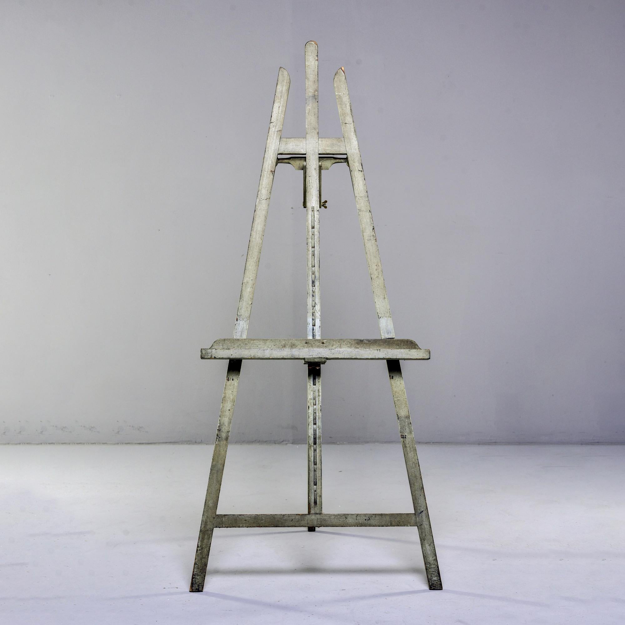 English wooden standing easel with gray green painted finish, circa 1930s.

Depth folded: 6”
Depth fully extended: 57”
Tray shelf is adjustable.
  