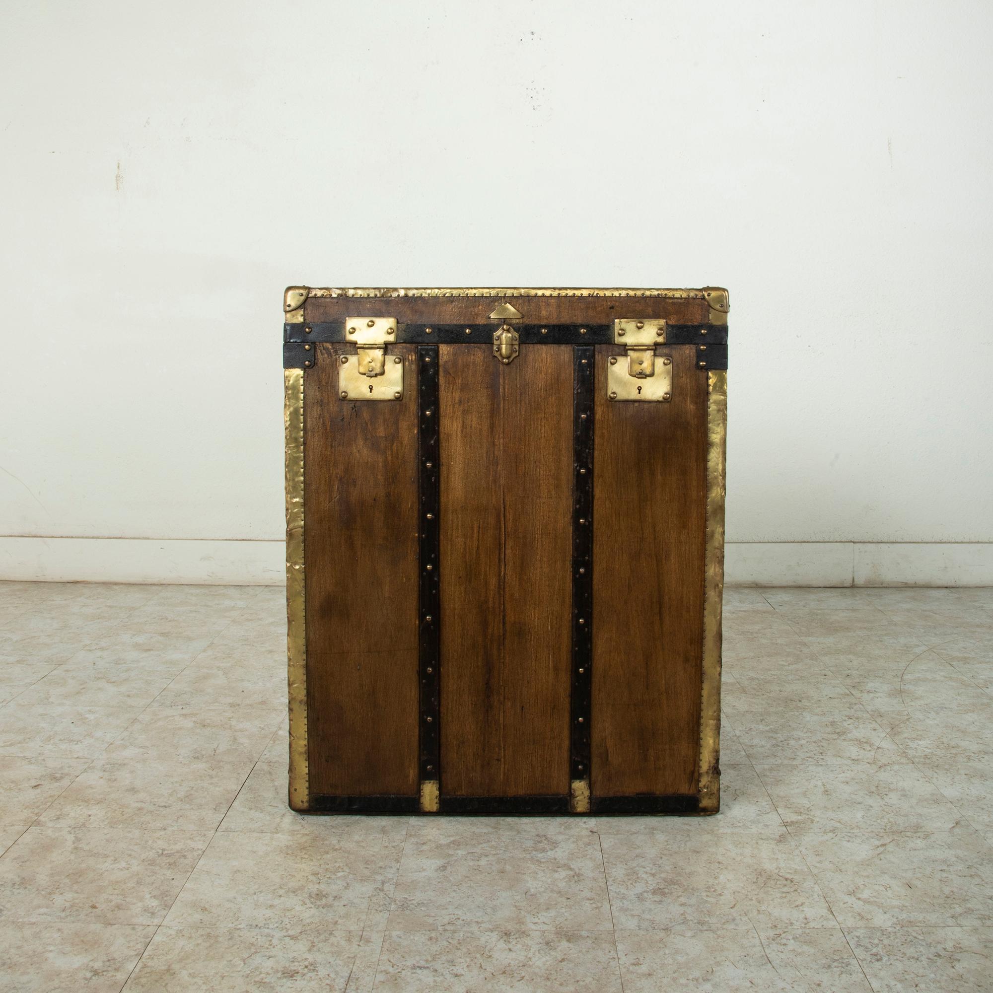 Standing at 34 inches in height, this tall early-20th century French beech wood steamer trunk features wooden runners with brass rivets and brass corners and edges. Iron straps surround the lid and base. Leather handles on the sides allow for easier