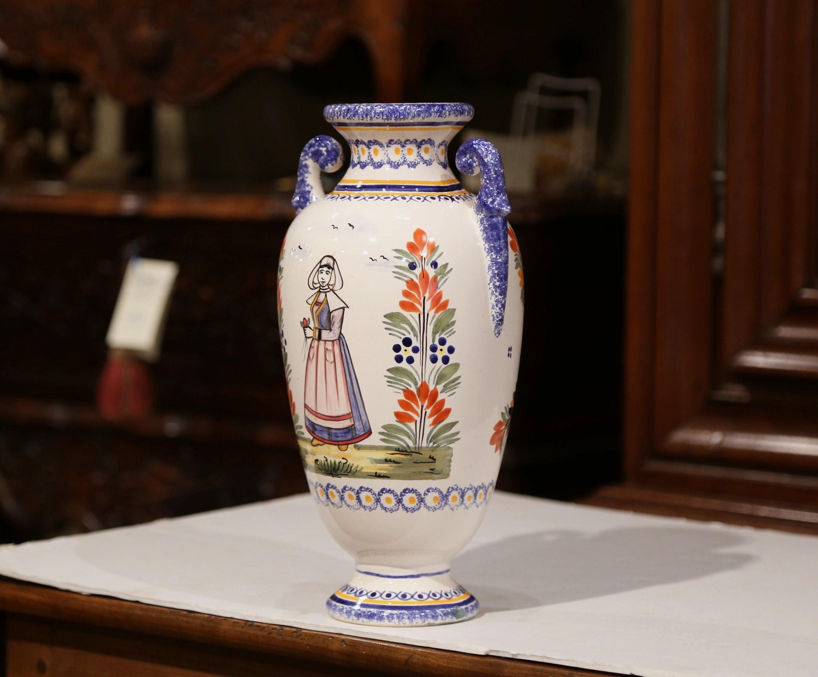 This antique ceramic vase was created in Brittany, circa 1920. Round in shape, the faience piece has curved handles and features colorful hand painted decor. The painted elements include a Breton woman dressed in traditional, historically accurate