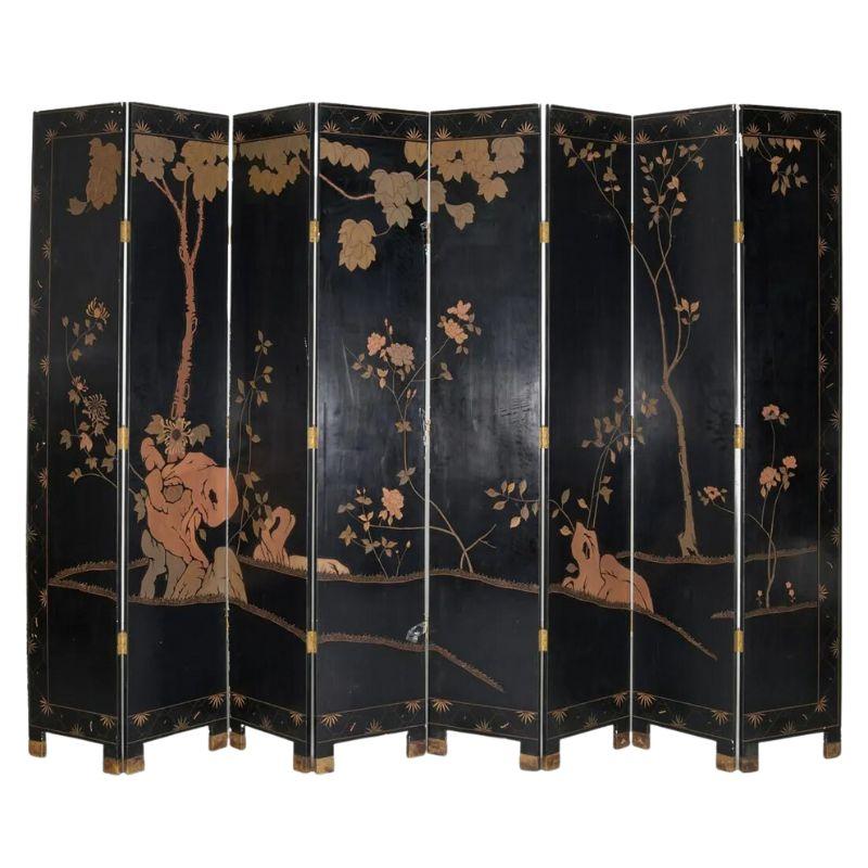 A tall, eight panel lacquered coromandel Chinese screen. Crafted of enamel and black lacquer, decorated with figures in a court setting. Reverse side depicts flowering plants.  Panels are raised on brass, capped feet and joined by brass hinges. 