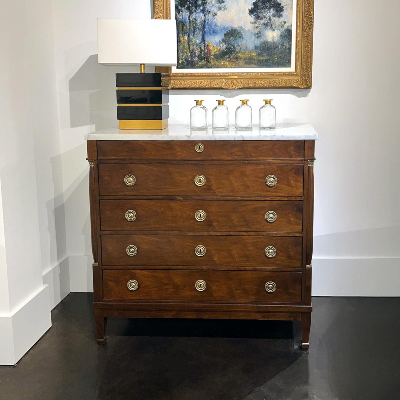 La cassettiera sfoggia una grandeur in stile Impero con impiallacciatura in noce e accenti in ottone massiccio. Il suo classico piano in marmo bianco aggiunge un tocco di lusso, rendendolo un punto focale di grande effetto.

Con colonne