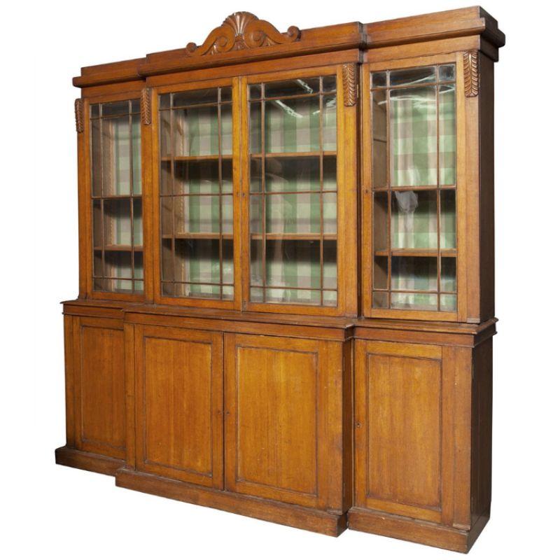 A vintage oak English oak breakfront cabinet with glass doors, and a scroll and shell form center pediment. Carved leaf details adorn the top door corners.  The bookcase cabinet has four glass doors with divided light panes in the top half, each