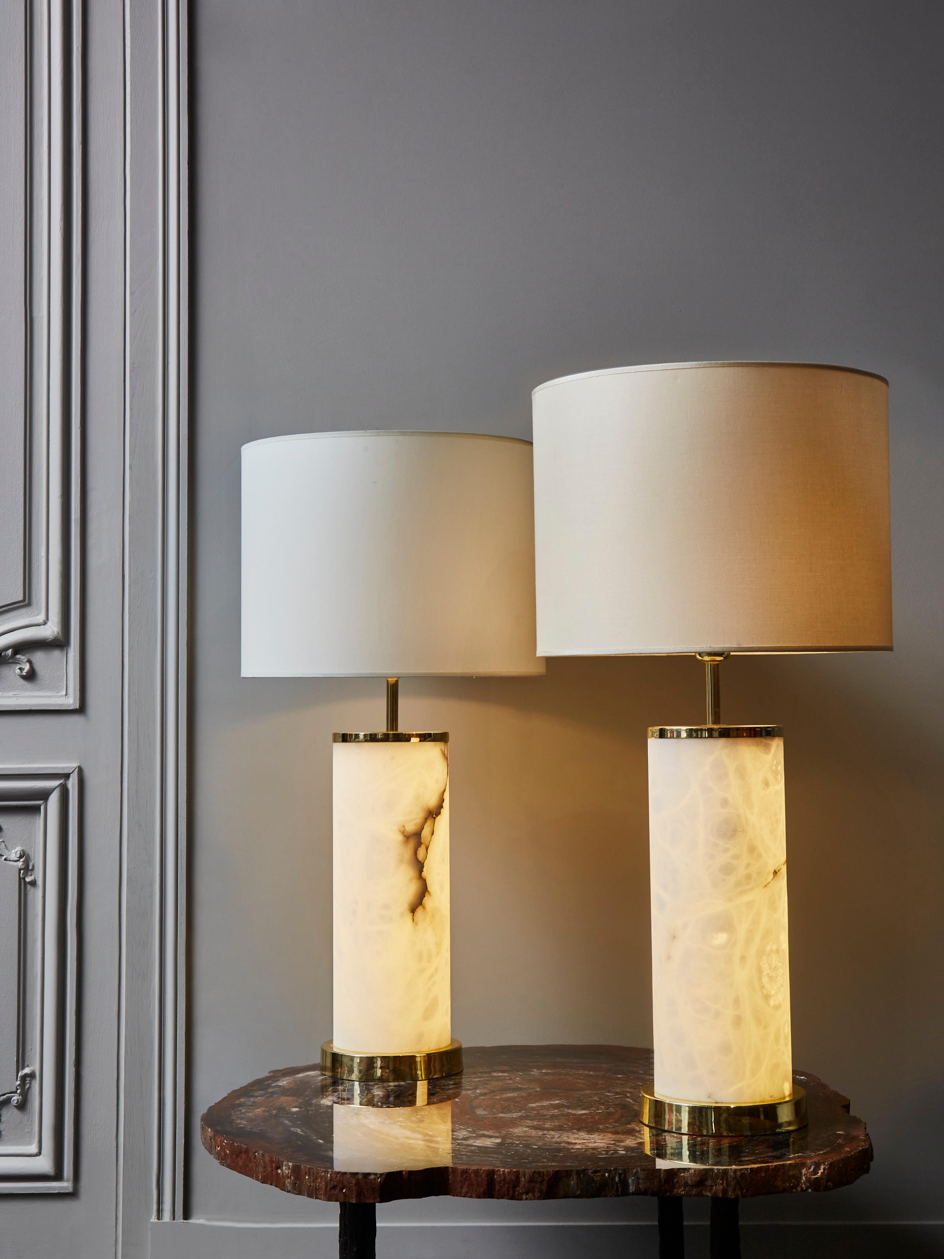 Pair of brass and alabaster table lamps by Glustin Luminaires.

Tall enlightened alabaster cylinders, set by alabaster feet and upper ring.