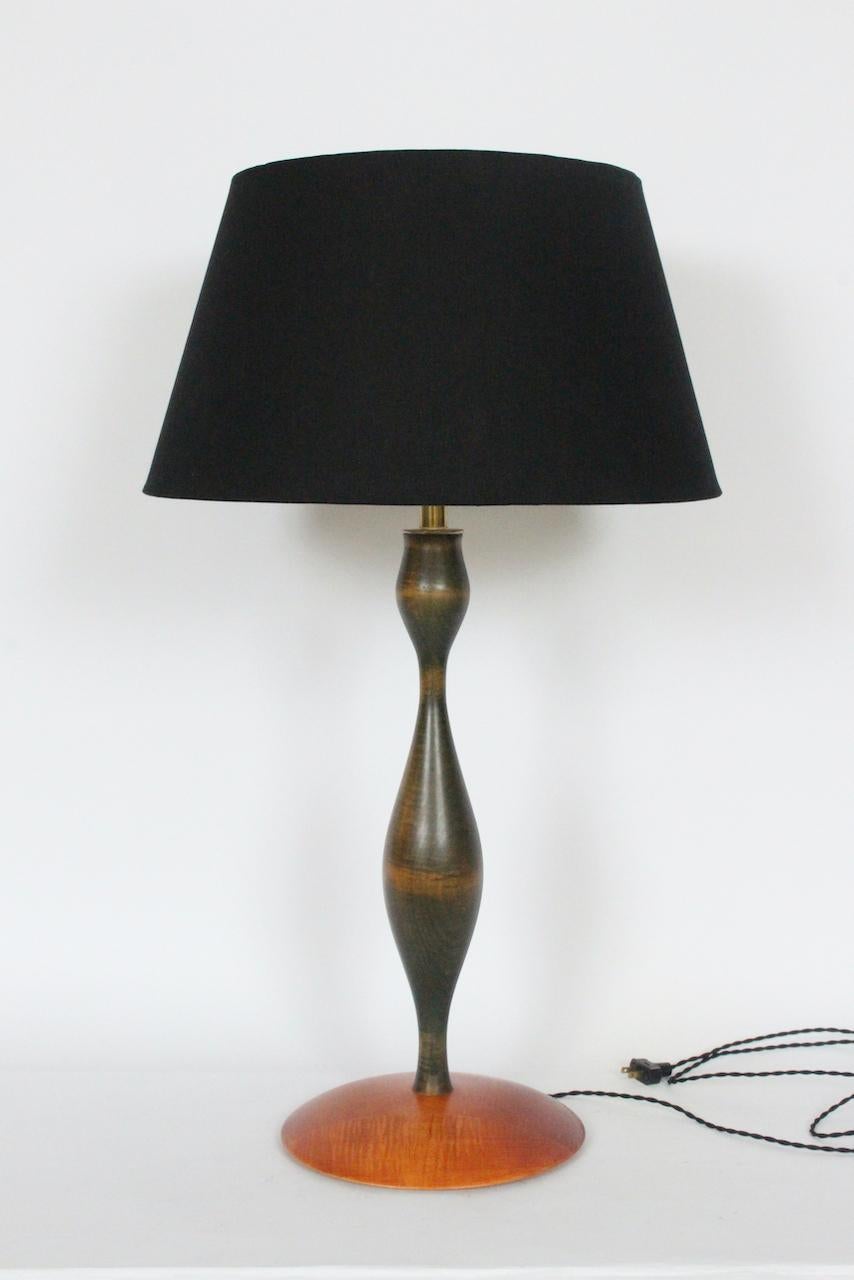 High Eva Zeisel, RB Universal Woodworks produced Maple Table Lamp, 1999. Featuring her classic slender, smooth corseted form in turned two toned stained hardwood with Charcoal to light Brown body coloration atop a 11D staved Flame Maple disc base.