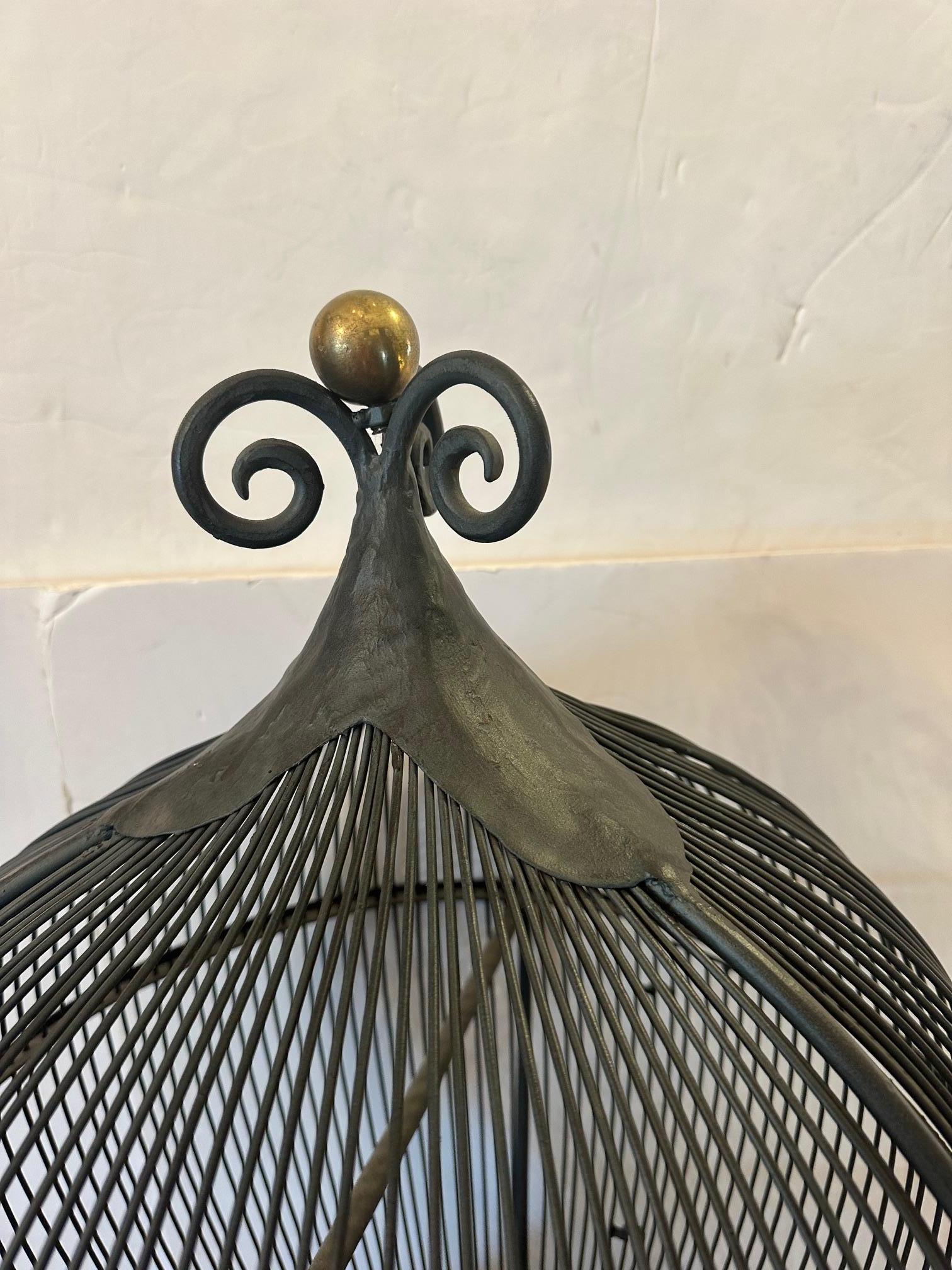 
Cage à oiseaux fantaisiste en fer noir sur pied, étonnante et inhabituelle, ayant 
2 perches, plateau rond amovible et bouton à bille en laiton sur le plateau et le dessus.  Merveilleuse forme sculpturale.

GG