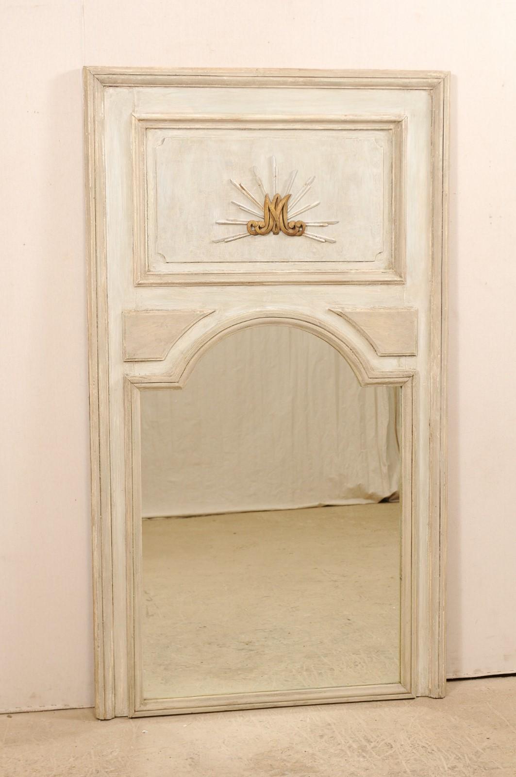A tall French painted wood trumeau mirror from the 19th century. This antique mirror from France features the tall rectangular-shape, with typical trumeau design of wooden plaque-style top, above a glass mirror, with arch-shaped top. The upper panel