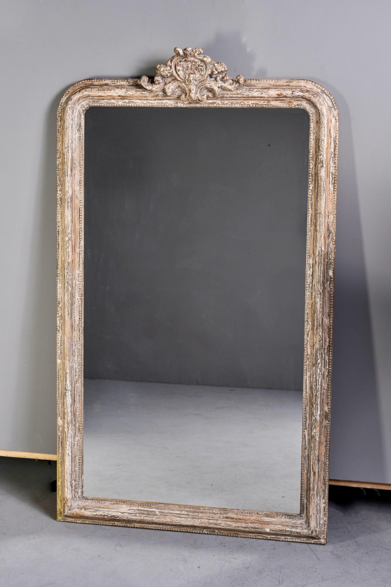 Louis Philippe mirror is five and half feet tall and features a white painted frame and carved crest, circa 1860s. Actual mirror size: 53.75” H x 30.25” W. Unknown maker.